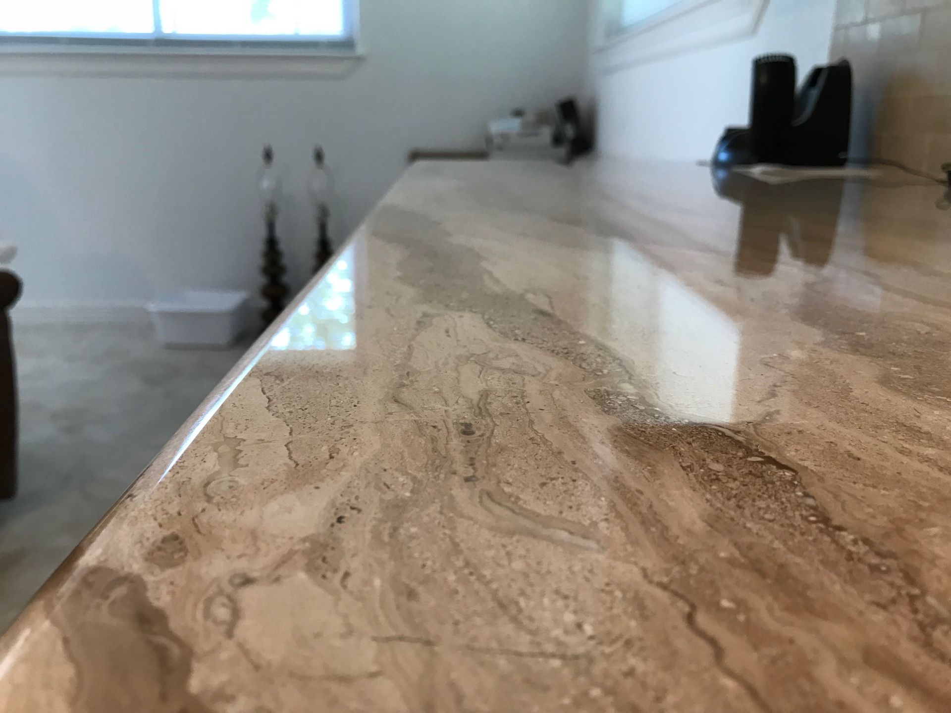 Reflective beige marble countertop in a bright kitchen with a window and a few small items in the background
