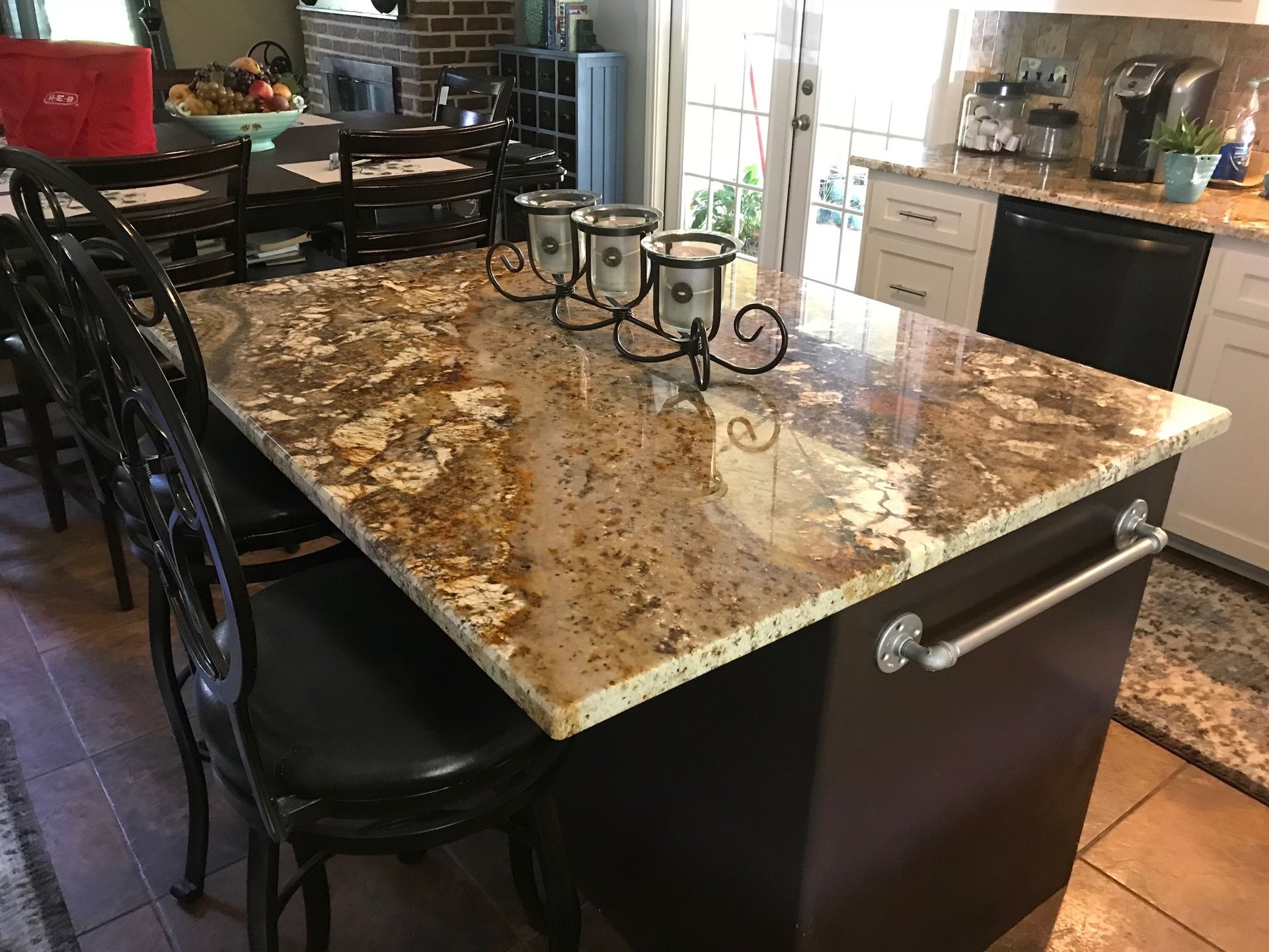 Kitchen island with brown granite countertop, black stools, and decorative metal candle holders