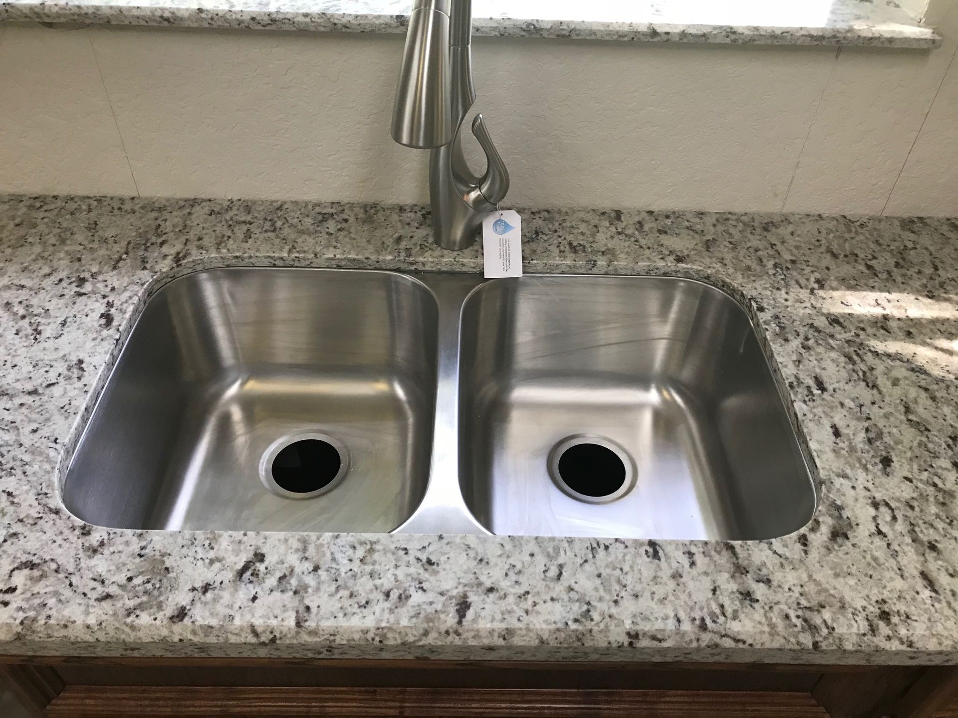 Stainless steel double kitchen sink with granite countertop and faucet under a window