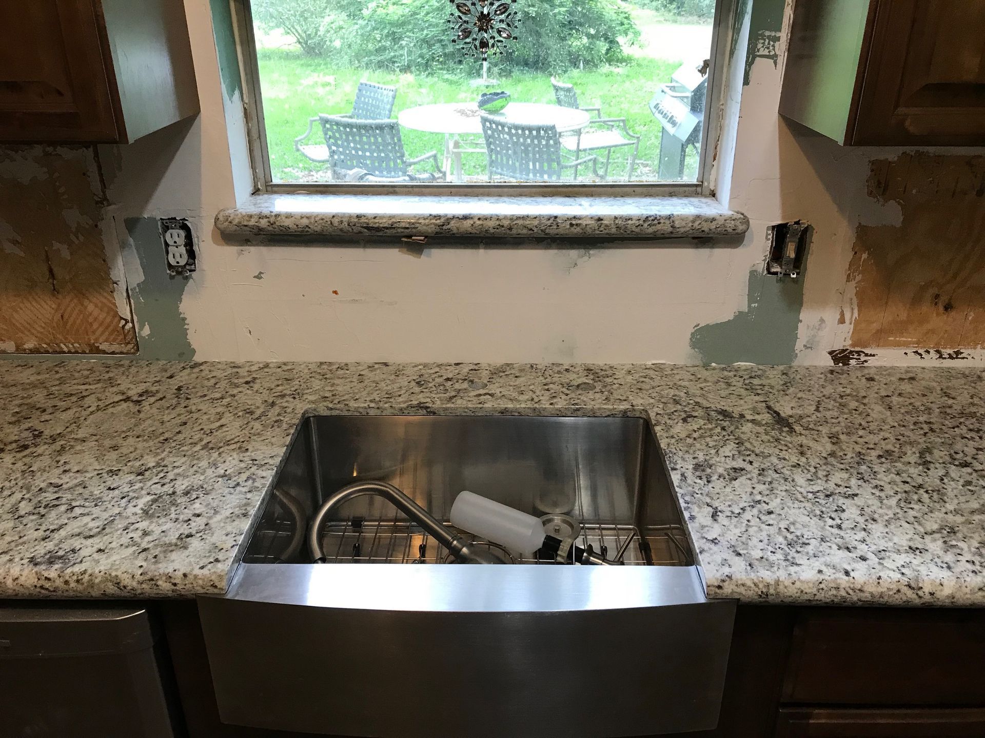 Kitchen counter with undermount sink beneath a window, showing a partially finished backsplash repair.