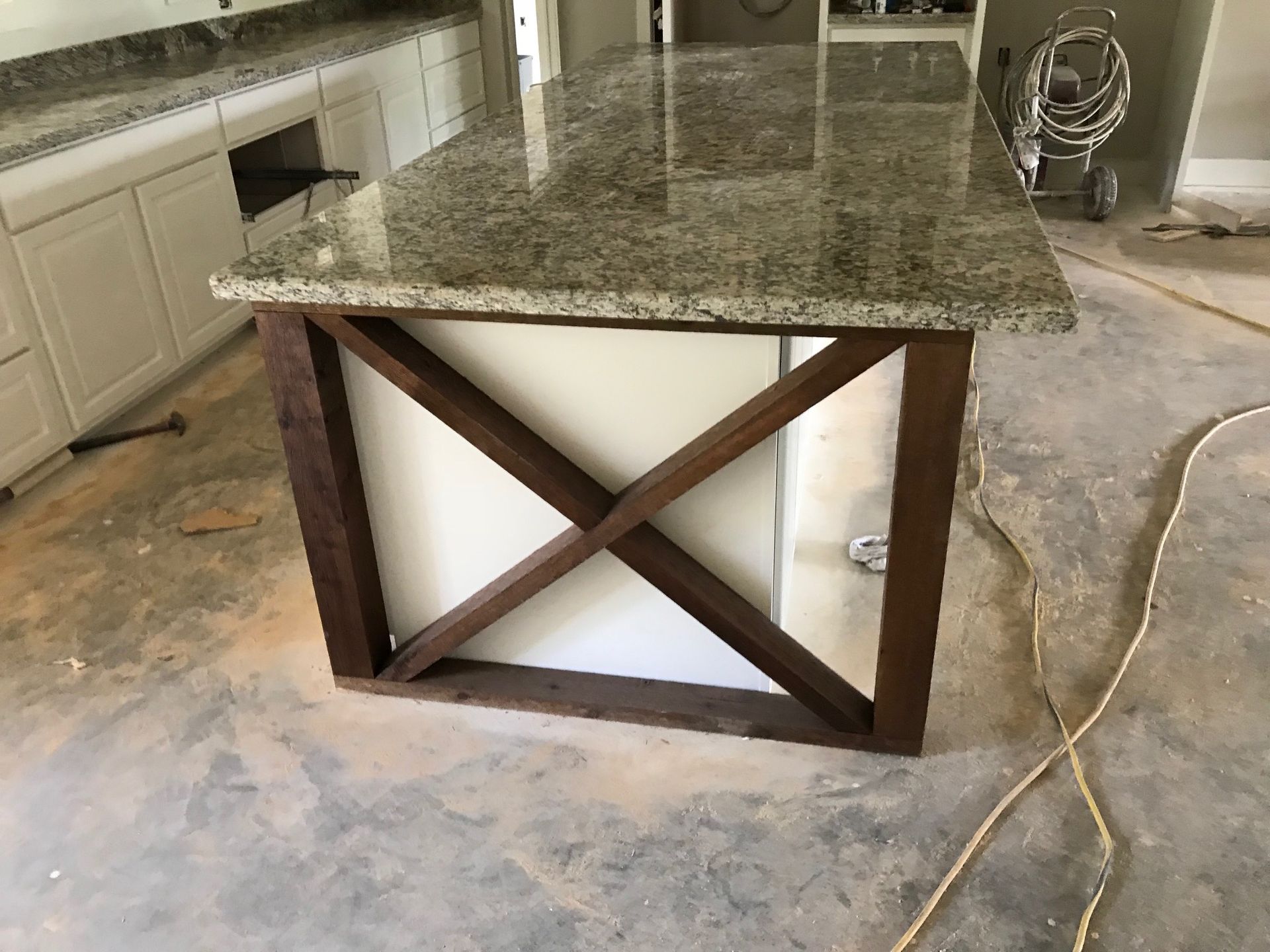 Kitchen island with granite countertop and brown cross-braced base on a concrete floor.