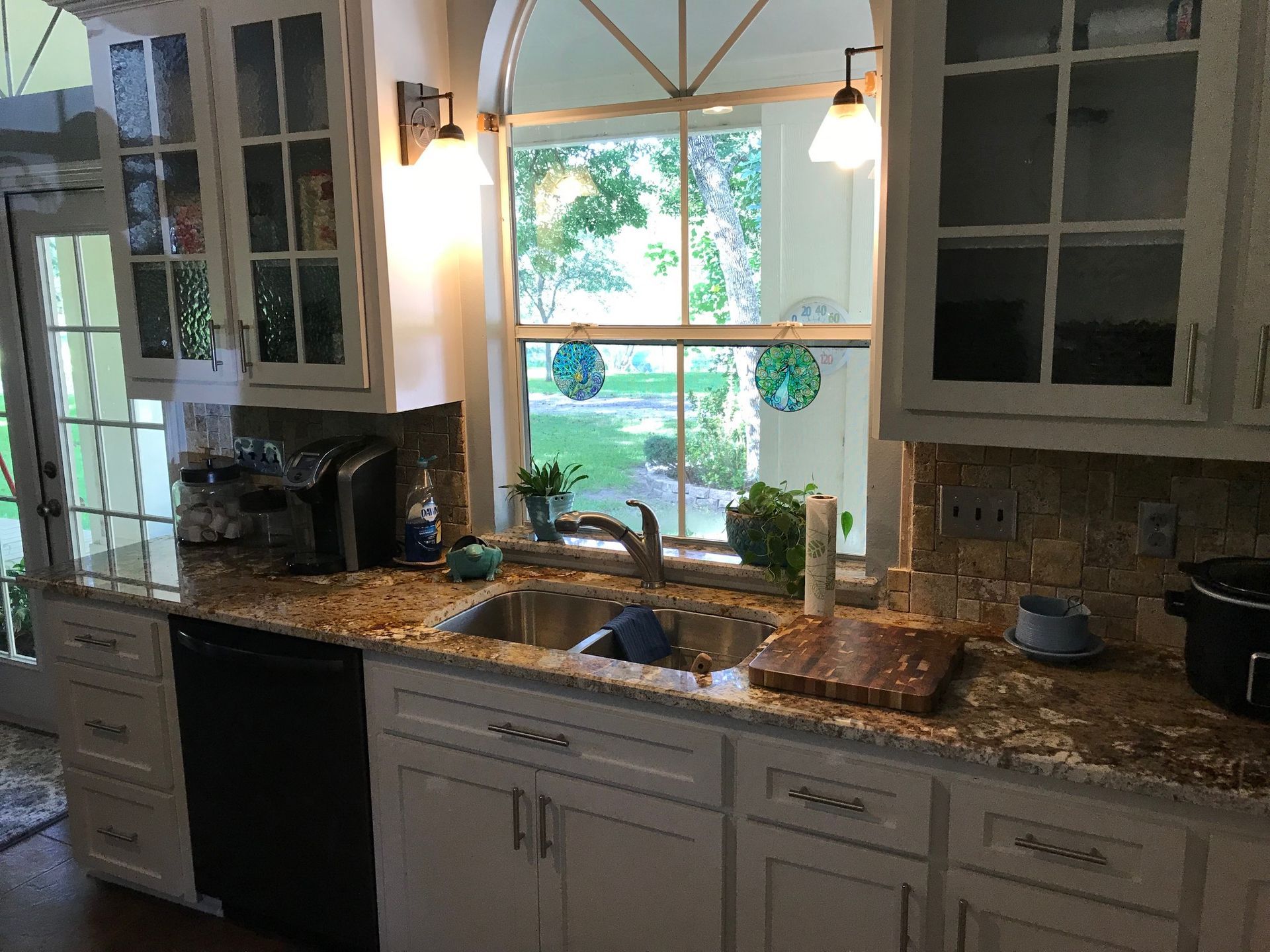 Bright kitchen sink area with white cabinets, granite counters, and a large window over the sink.