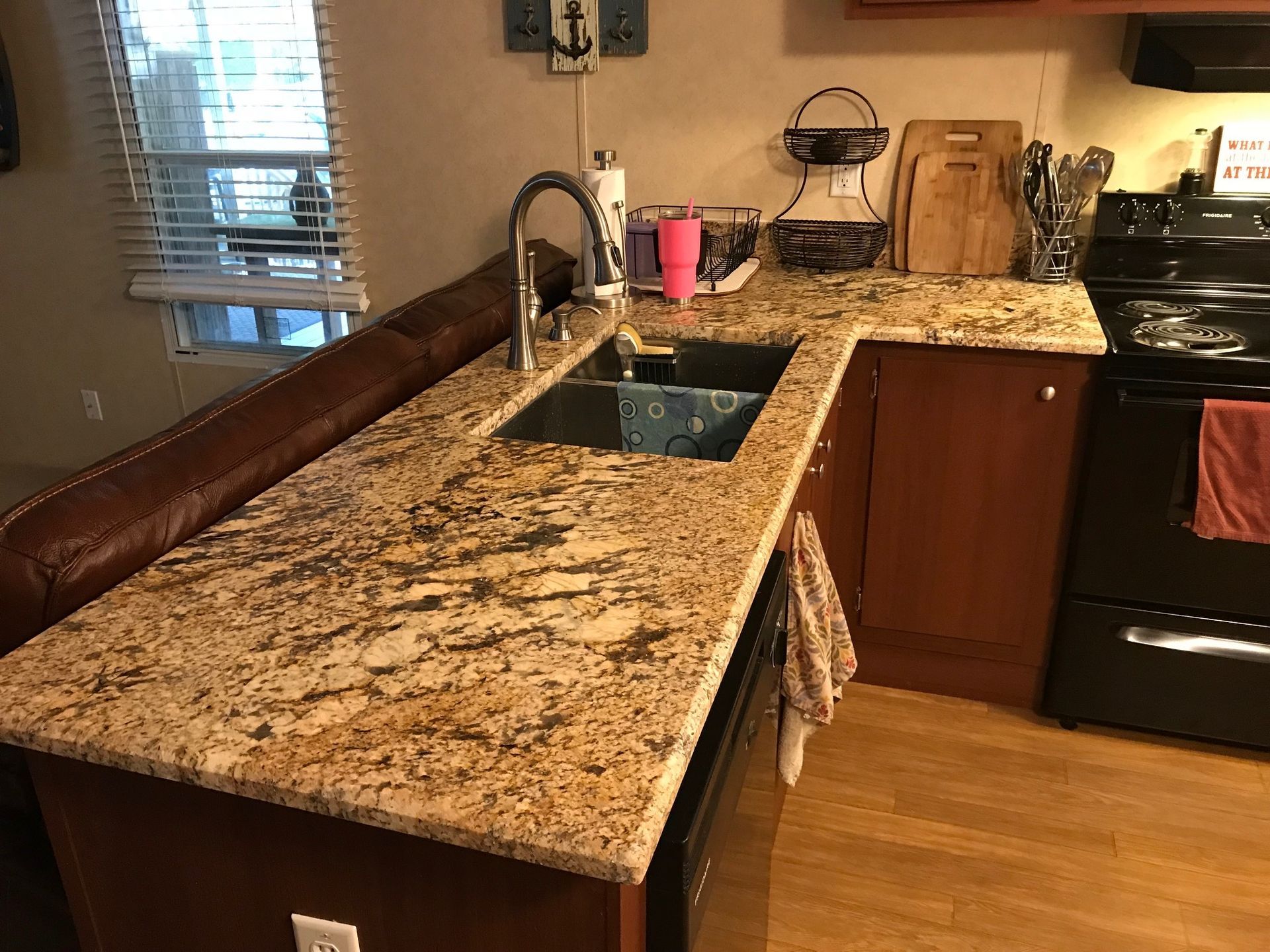 Granite kitchen countertop with sink, faucet, pink cup, and stove beside wooden cabinets and hardwood floor