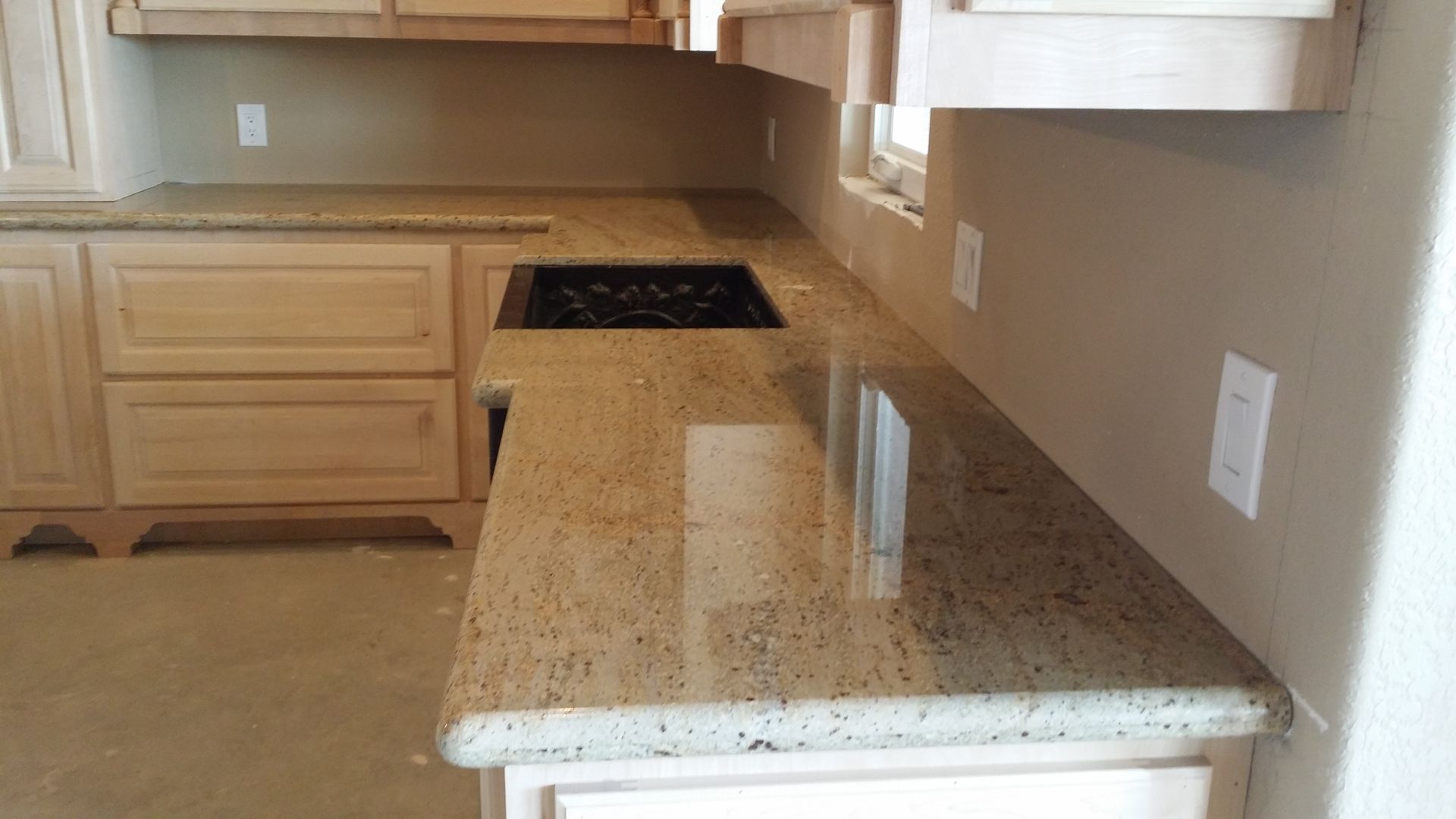 Empty kitchen with beige cabinets, speckled granite countertop, and built-in black cooktop.