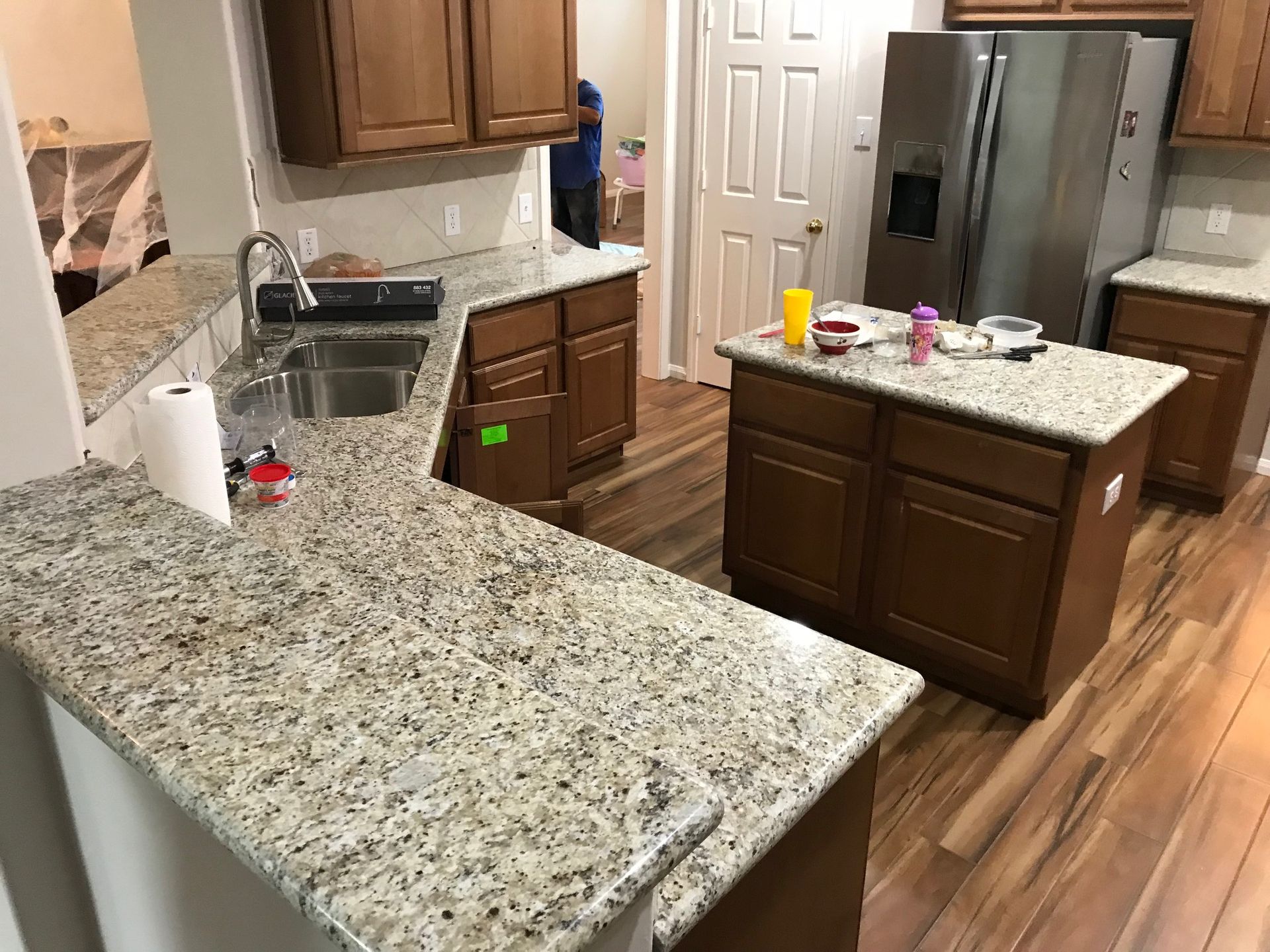 Kitchen with granite counters, brown cabinets, stainless sink, refrigerator, and wooden floor.
