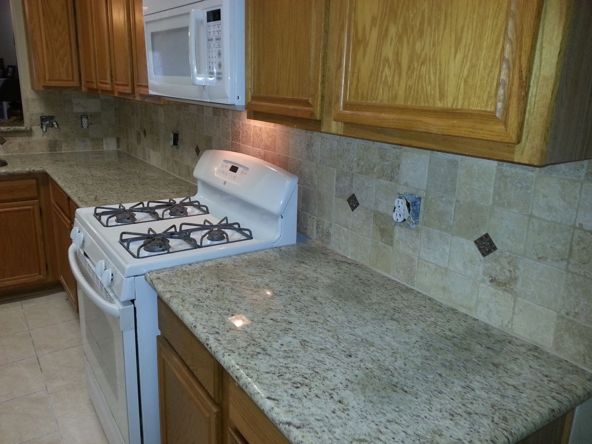 Kitchen with white gas stove, wood cabinets, and speckled granite countertop against tiled backsplash.