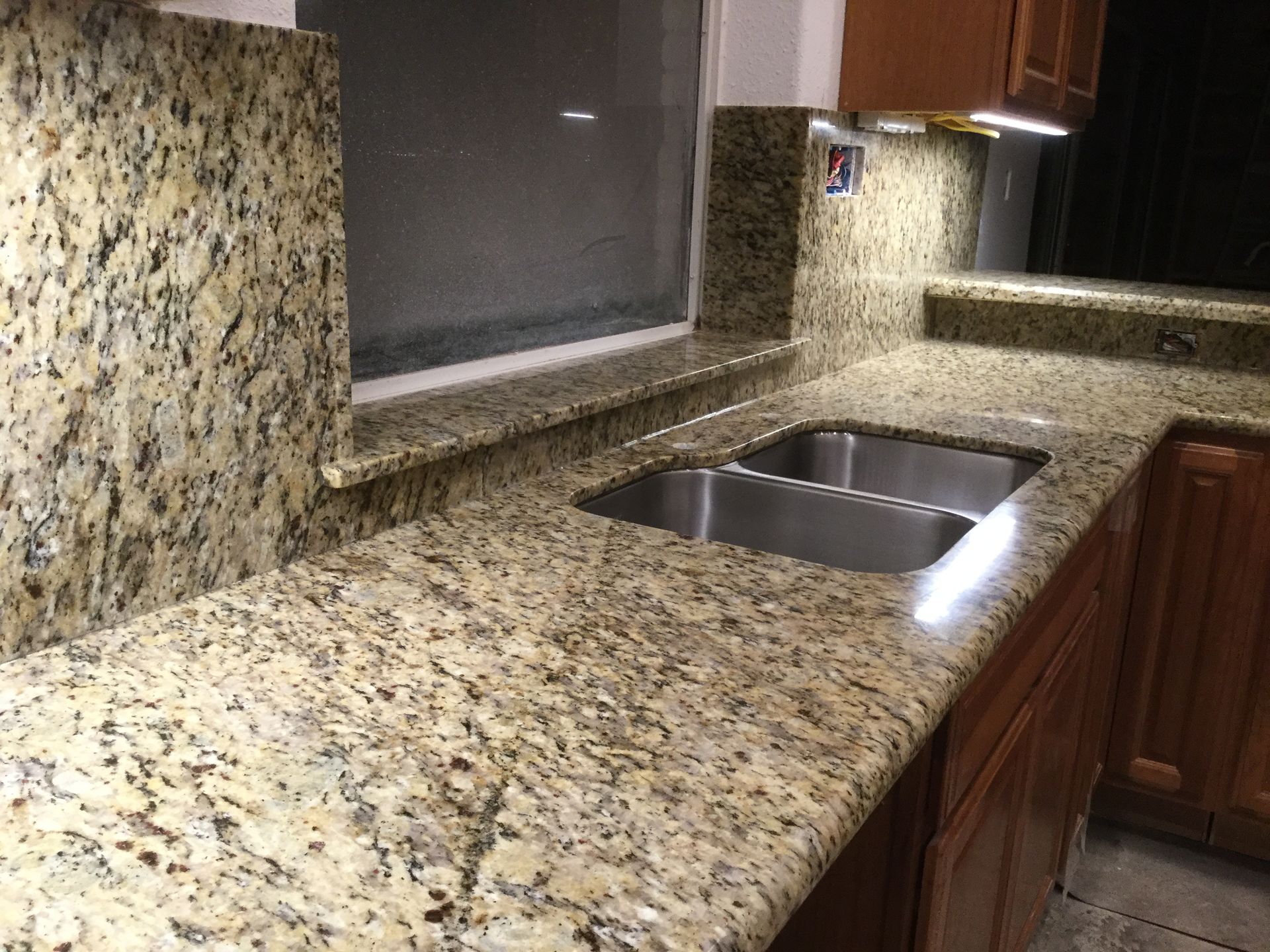 Granite kitchen countertop with double sink, wood cabinets, and tiled backsplash
