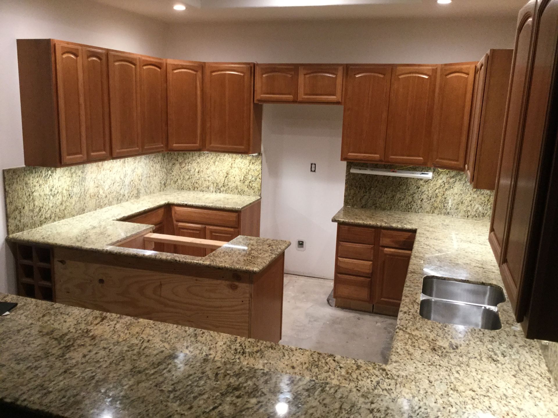 Empty kitchen with wood cabinets, granite counters, and a central island under recessed lighting