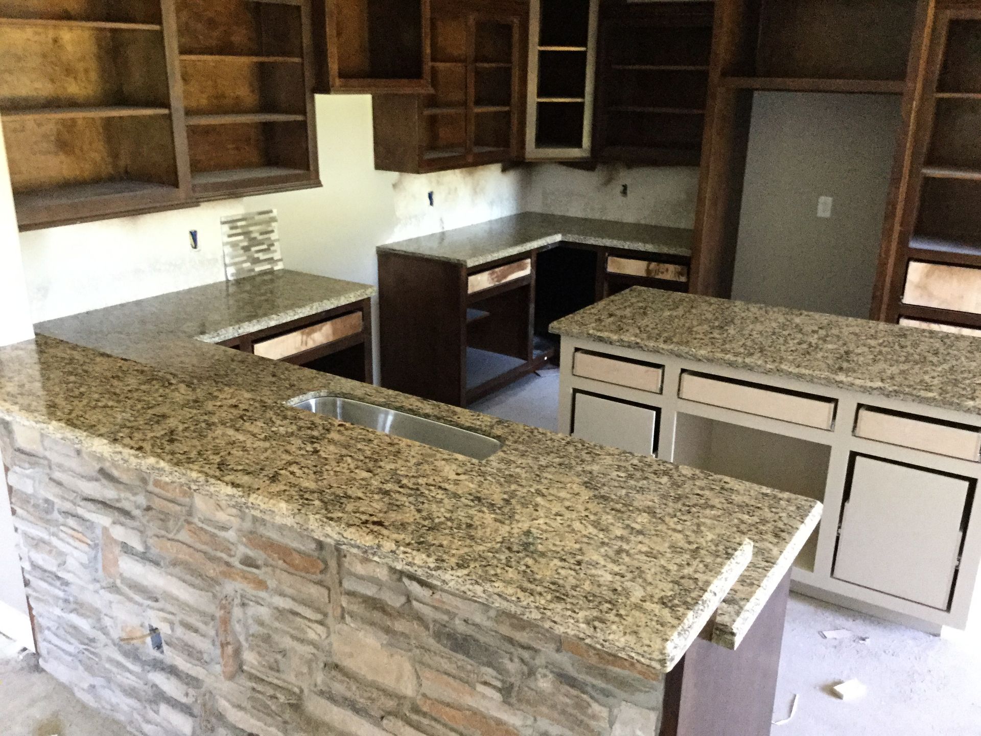 Empty kitchen with granite countertops, wood cabinets, and a stone-faced island.