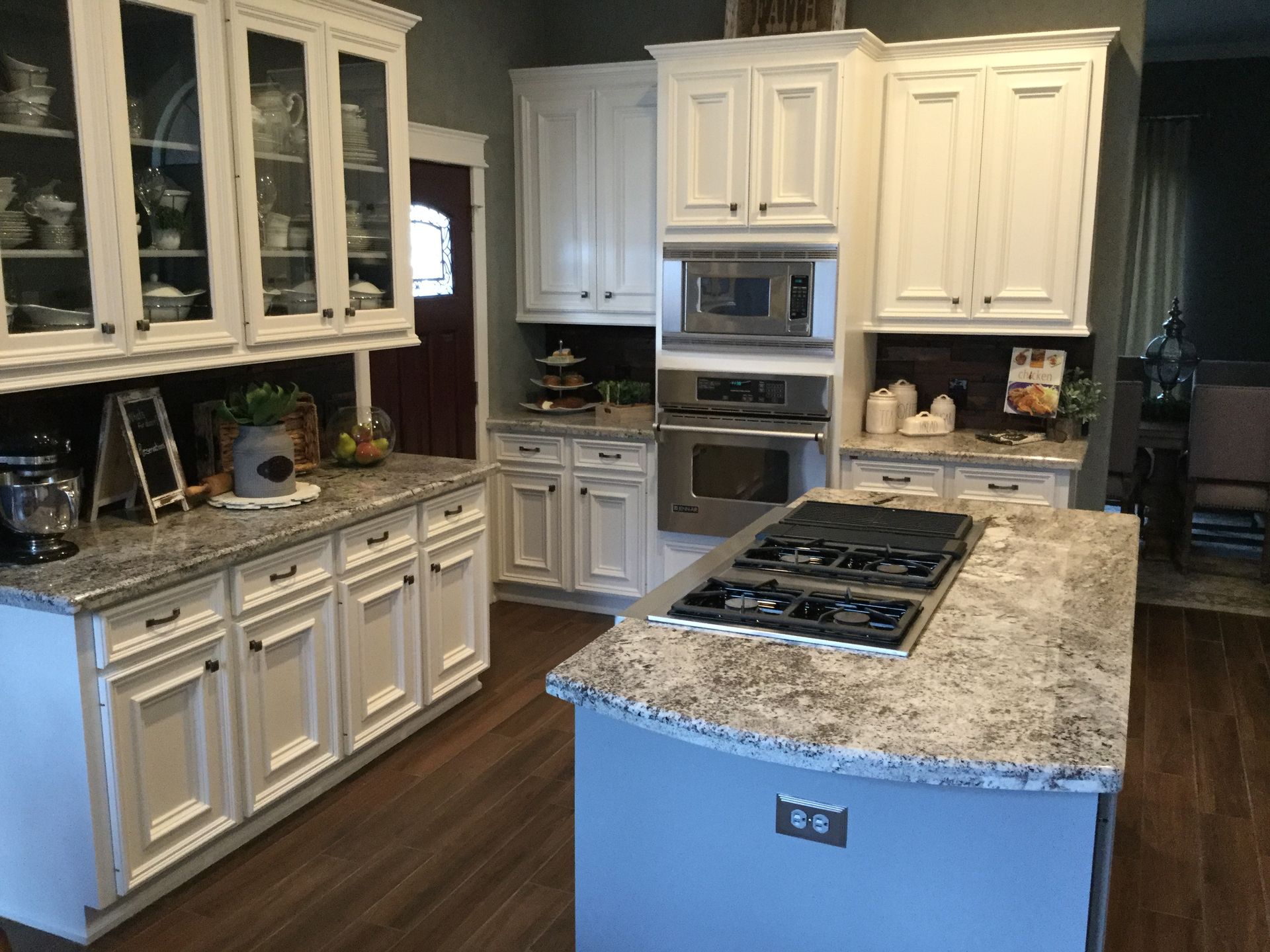 Bright kitchen with white cabinets, granite island, built-in oven, and hardwood floor
