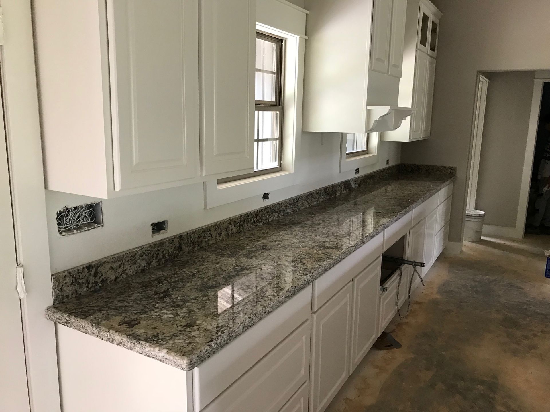 Kitchen with white cabinets and a long granite countertop along a bright wall.