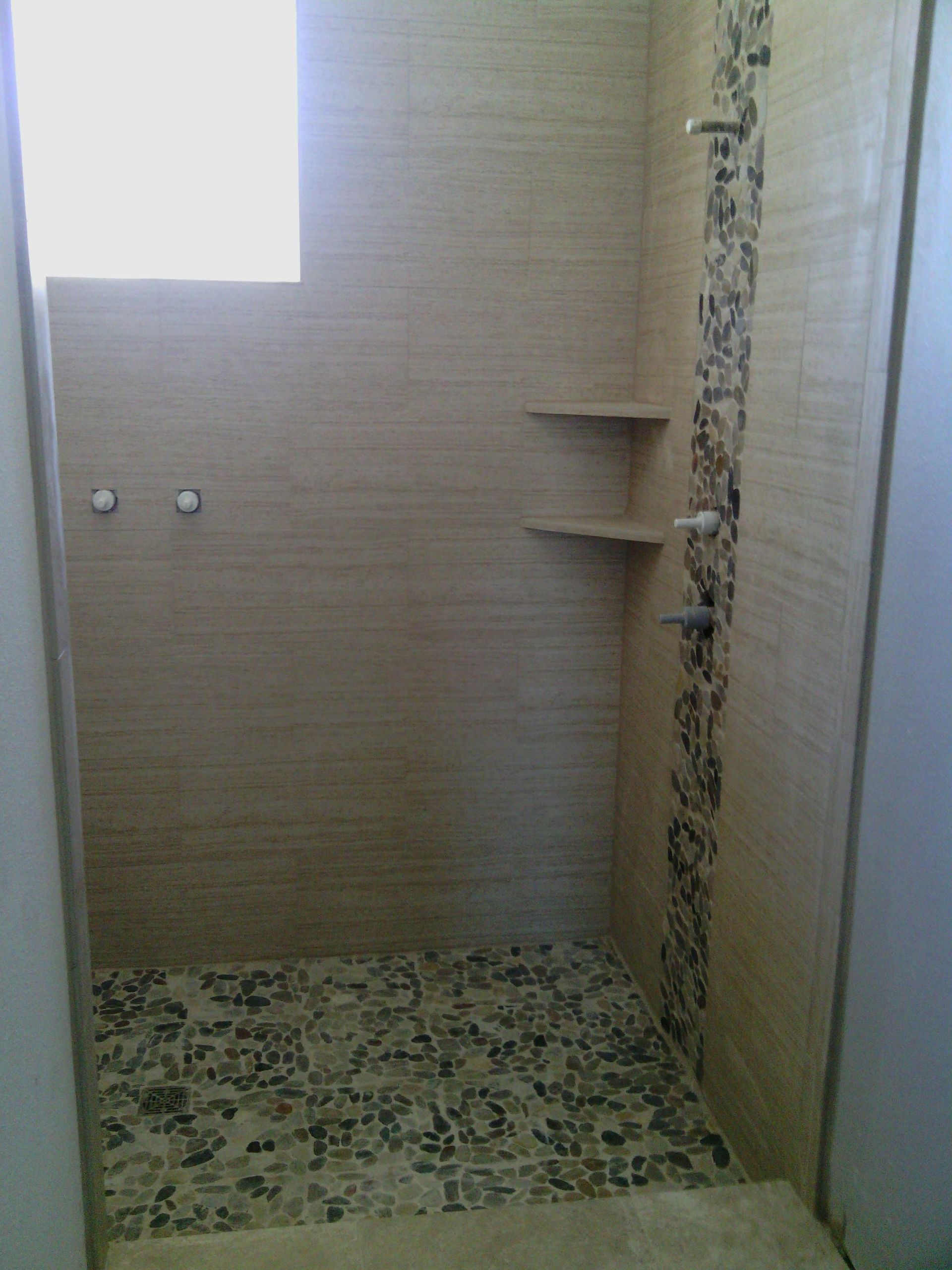 Small tiled shower stall with built-in corner shelves and frosted window light.
