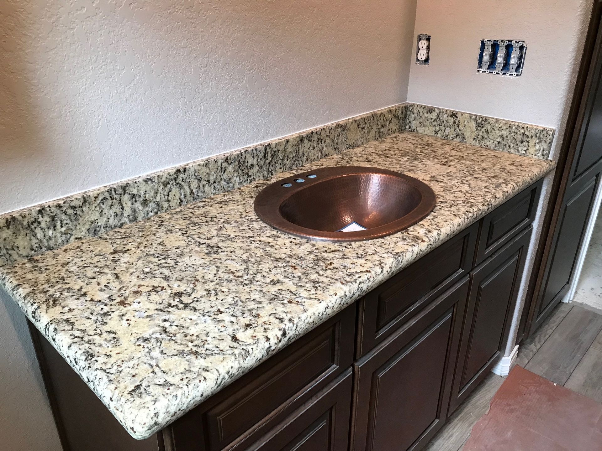Granite bathroom vanity with copper sink and dark wood cabinets against a beige wall.