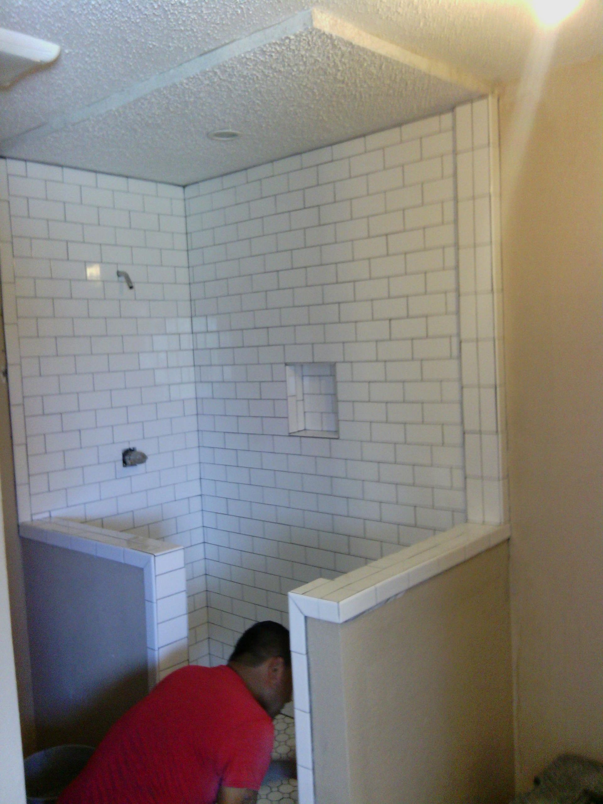 Partially tiled bathroom shower under renovation, with a worker crouched in the stall.