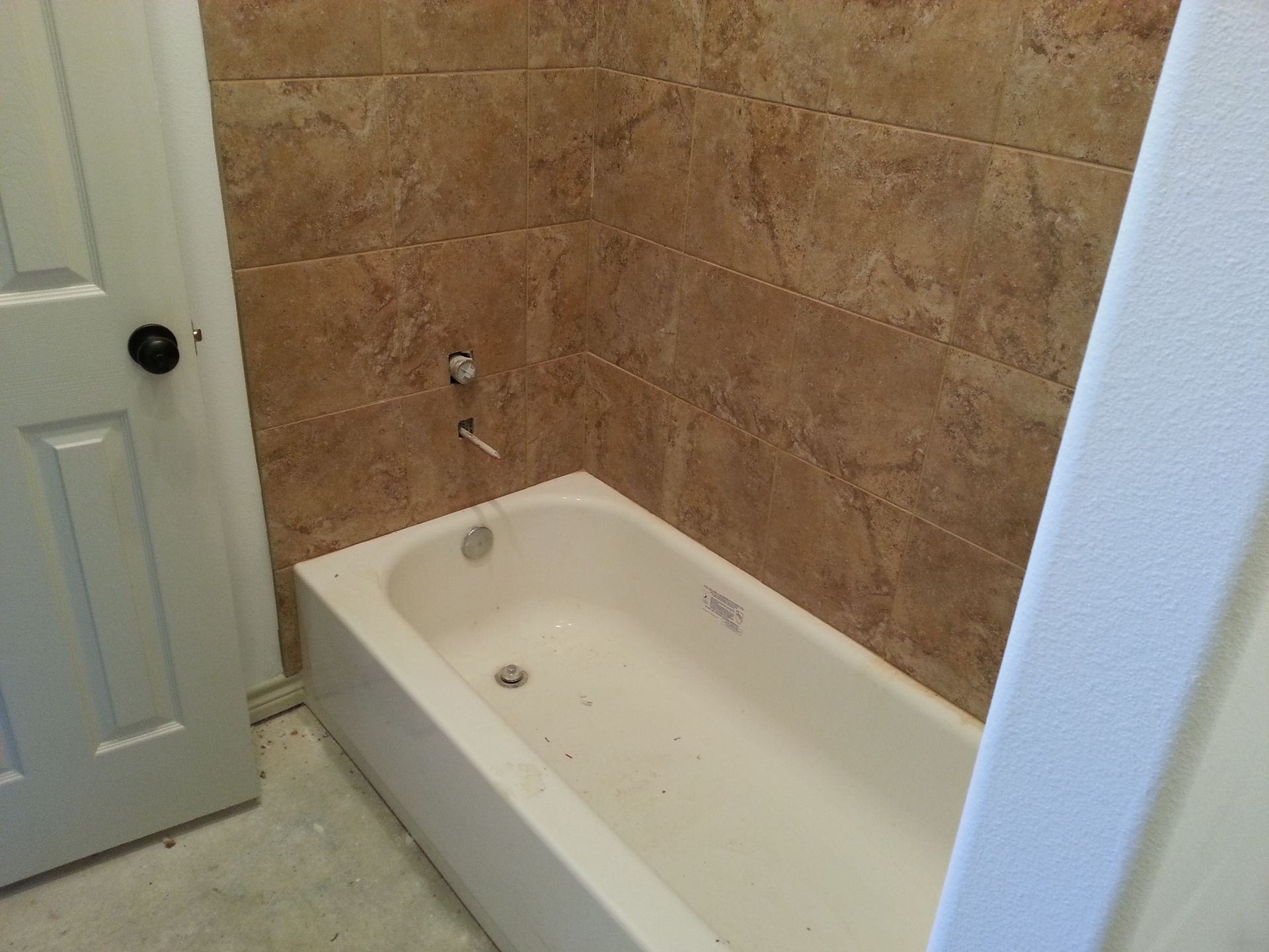 Small bathroom with a white bathtub and tan tiled walls beside a door.