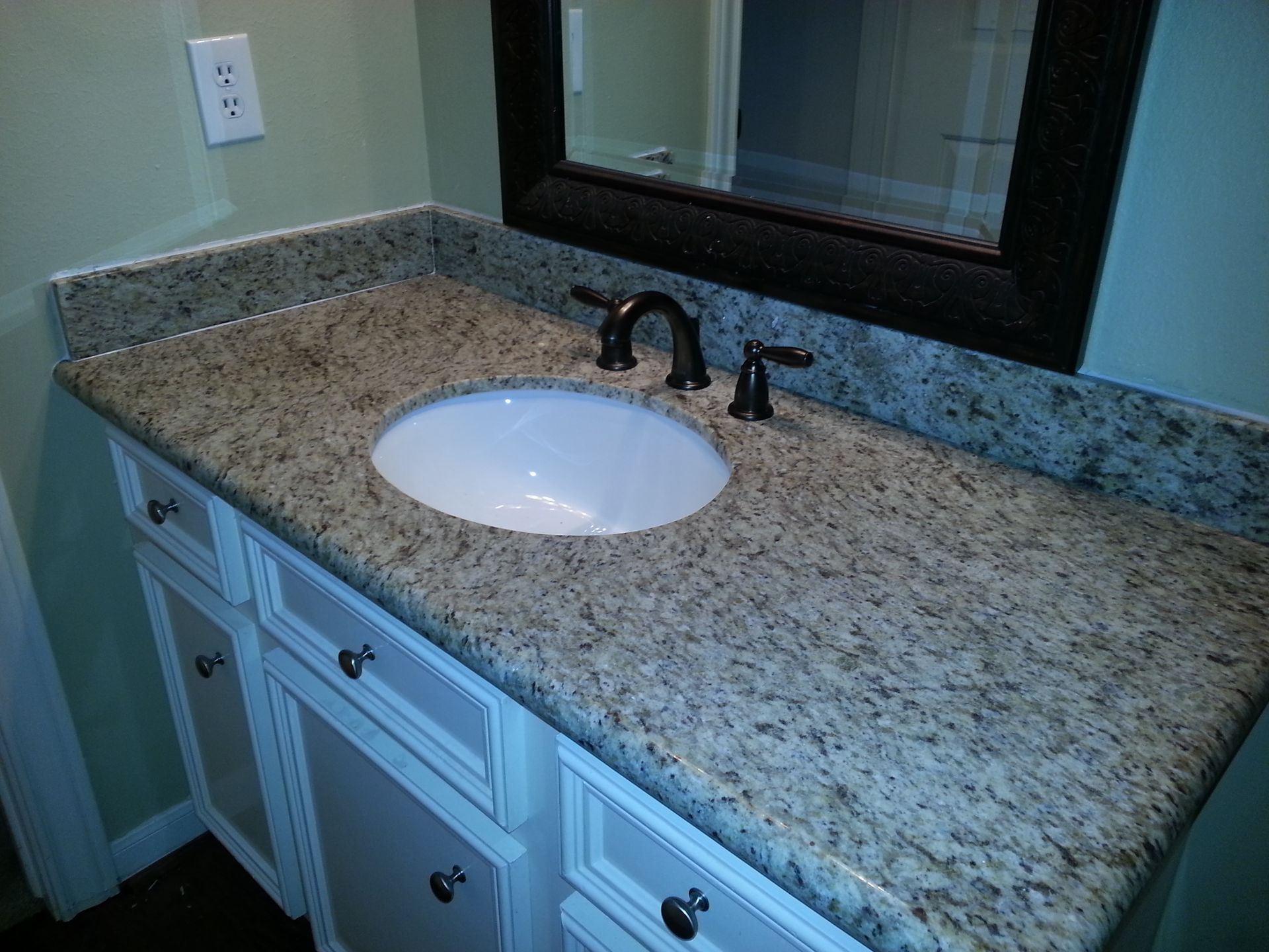 Bathroom vanity with granite countertop, round sink, and black faucet beneath a mirror.