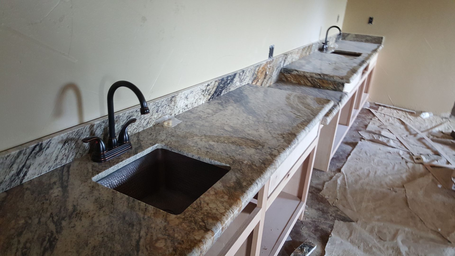 Damaged kitchen with long granite countertop, two sinks, and debris scattered across the floor.