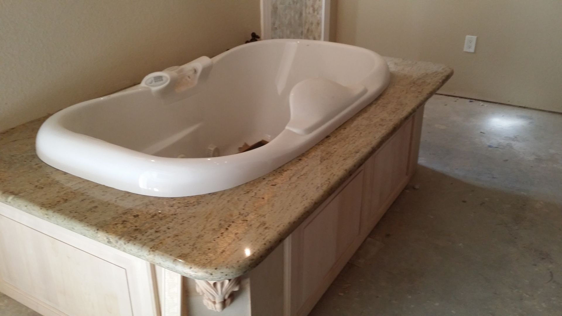 White soaking tub set into a tan granite bathroom vanity countertop, under construction.
