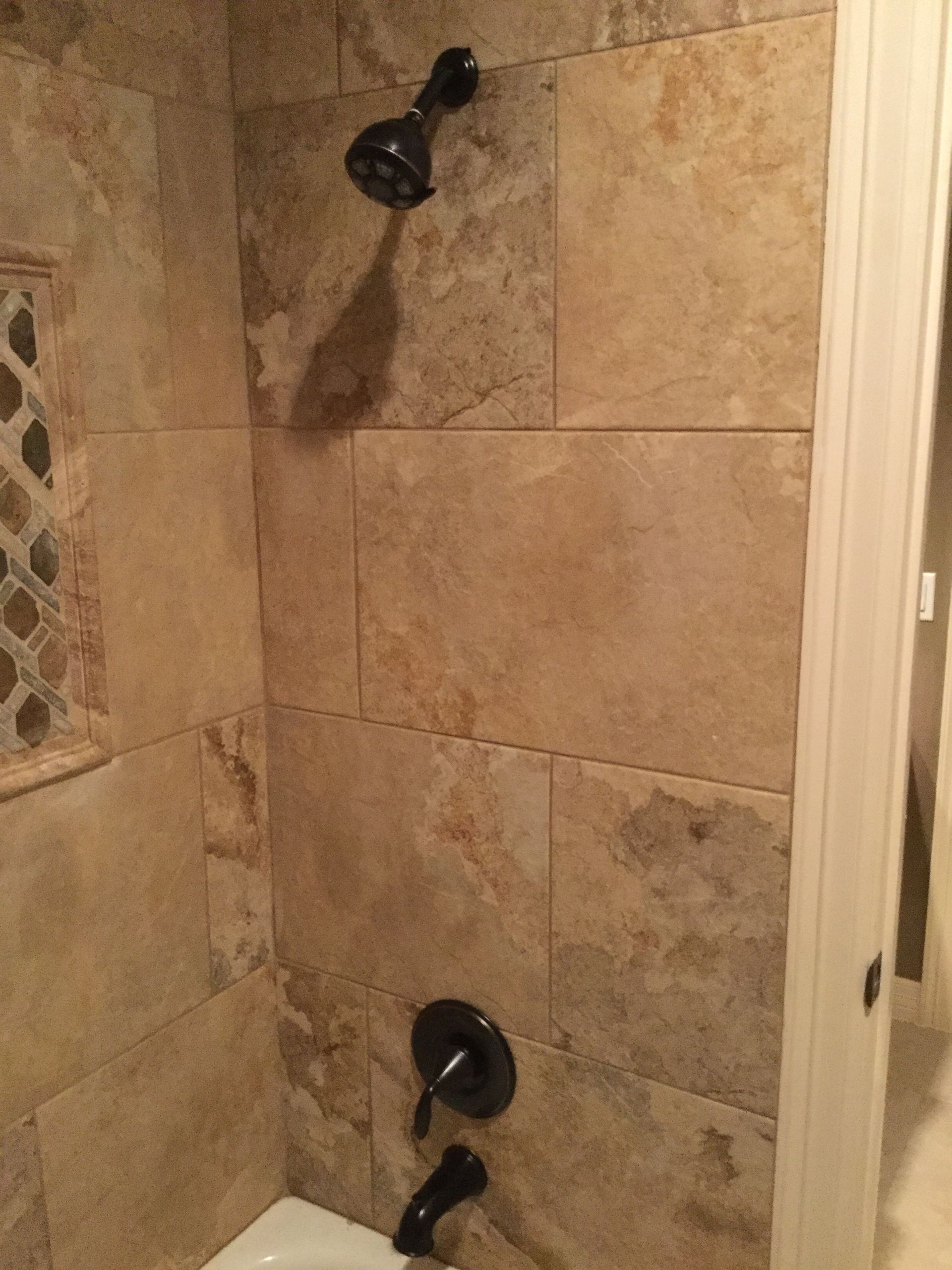 Corner shower with tan stone tile, black showerhead, and wall-mounted faucet handle
