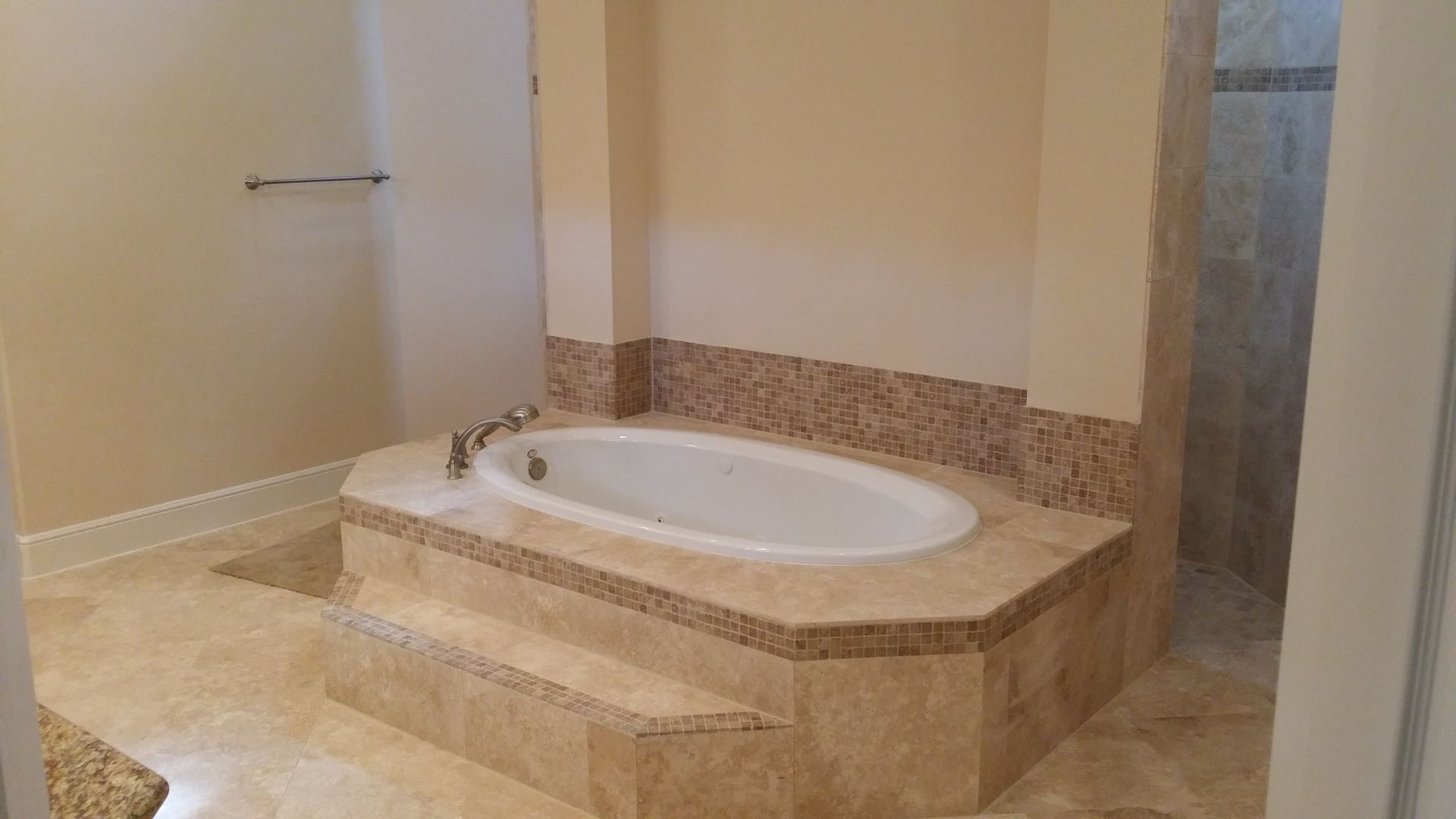 Luxury bathroom with a raised oval bathtub set in beige stone tile and a glass shower nearby