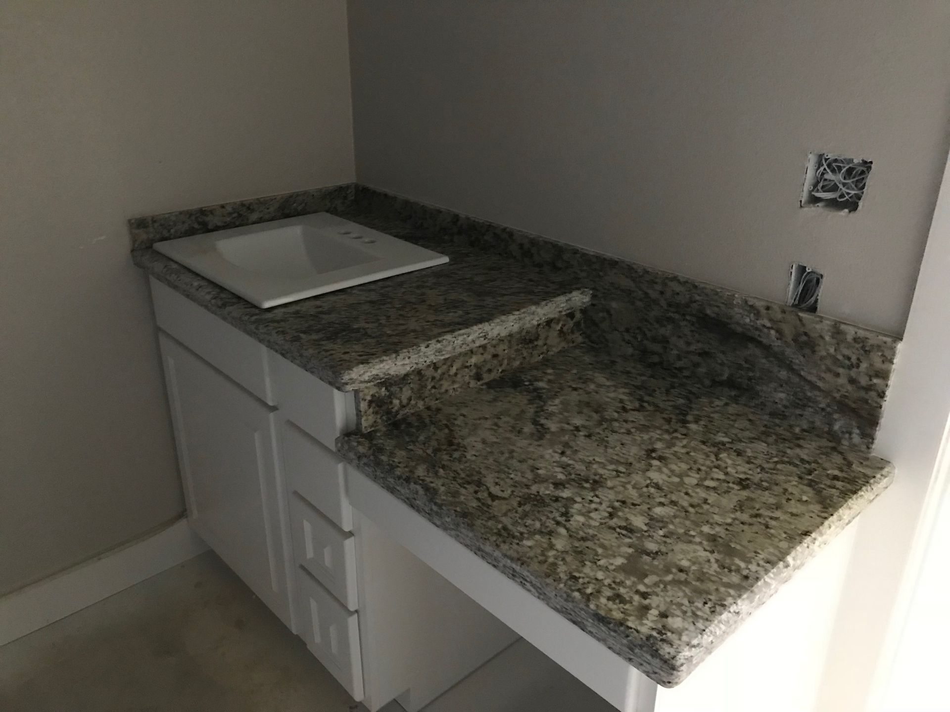 Unfinished bathroom vanity with granite countertop and white sink in a small corner nook