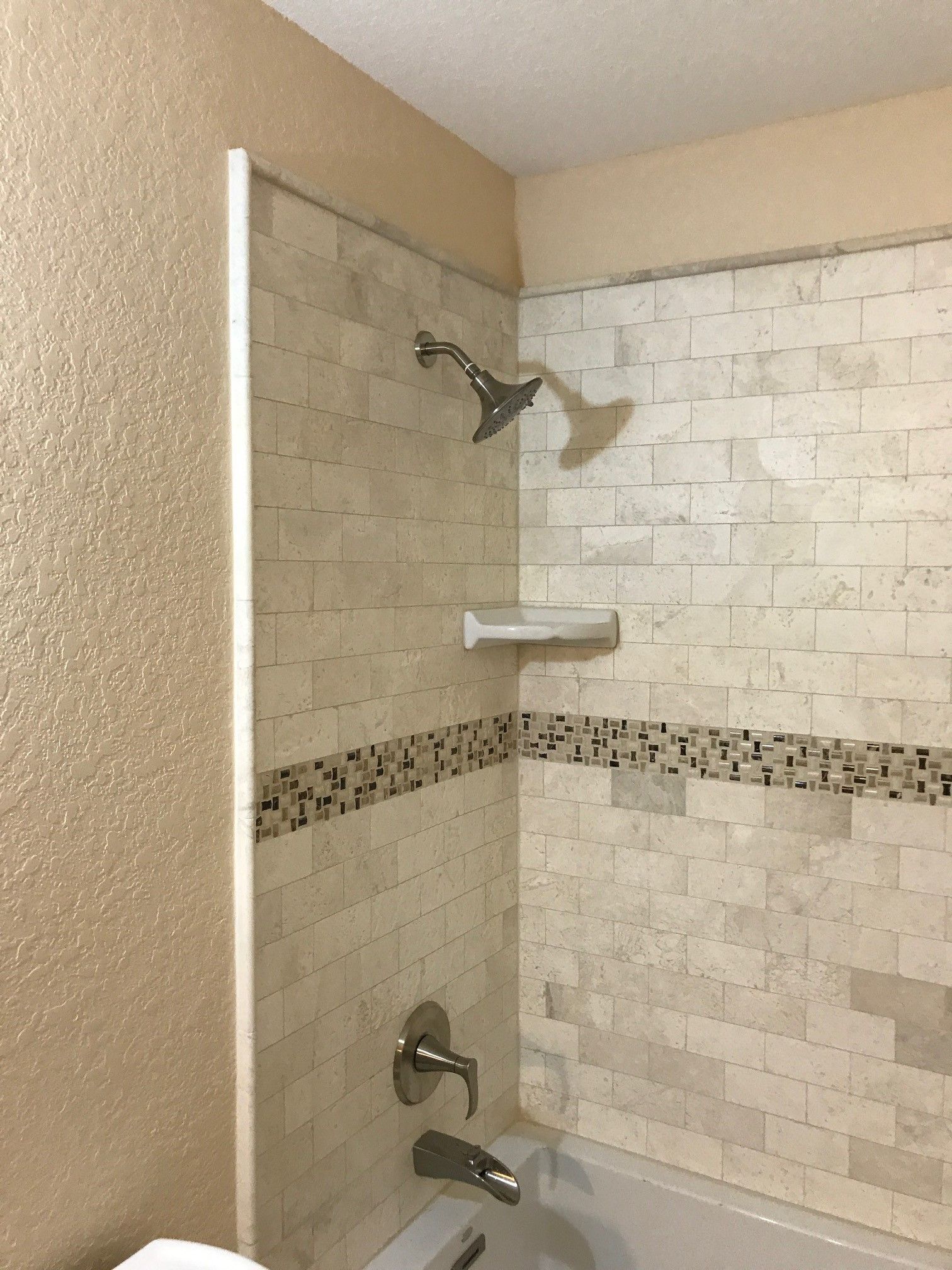 Walk-in shower with beige tile walls, glass panel, and chrome showerhead and fixtures.