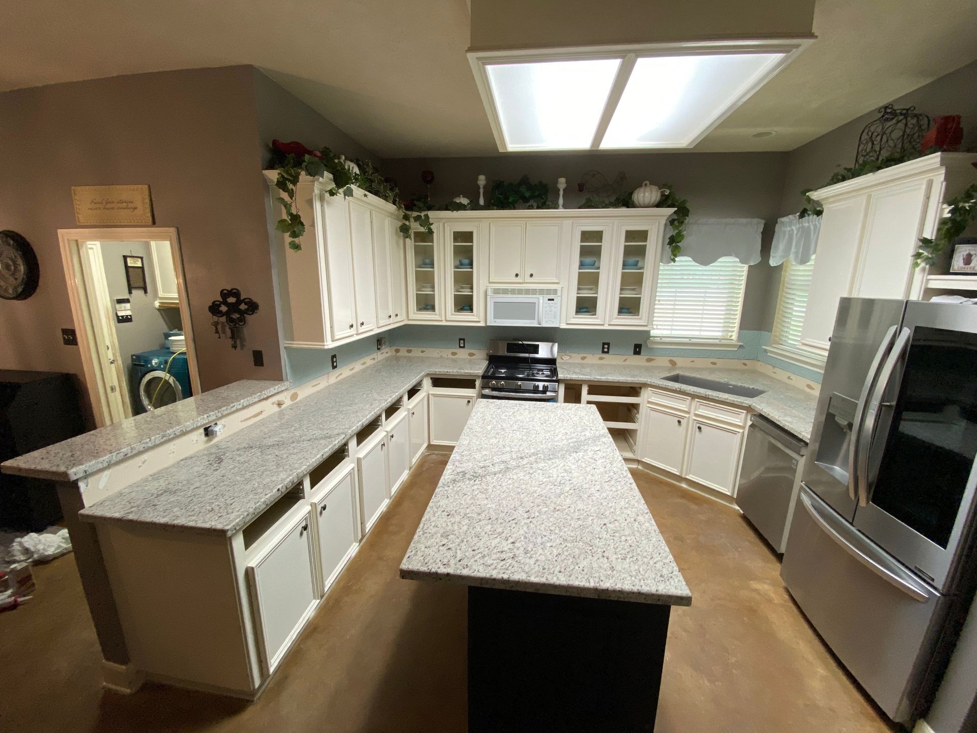 Bright kitchen with white cabinets, granite island, stainless appliances, and skylight overhead