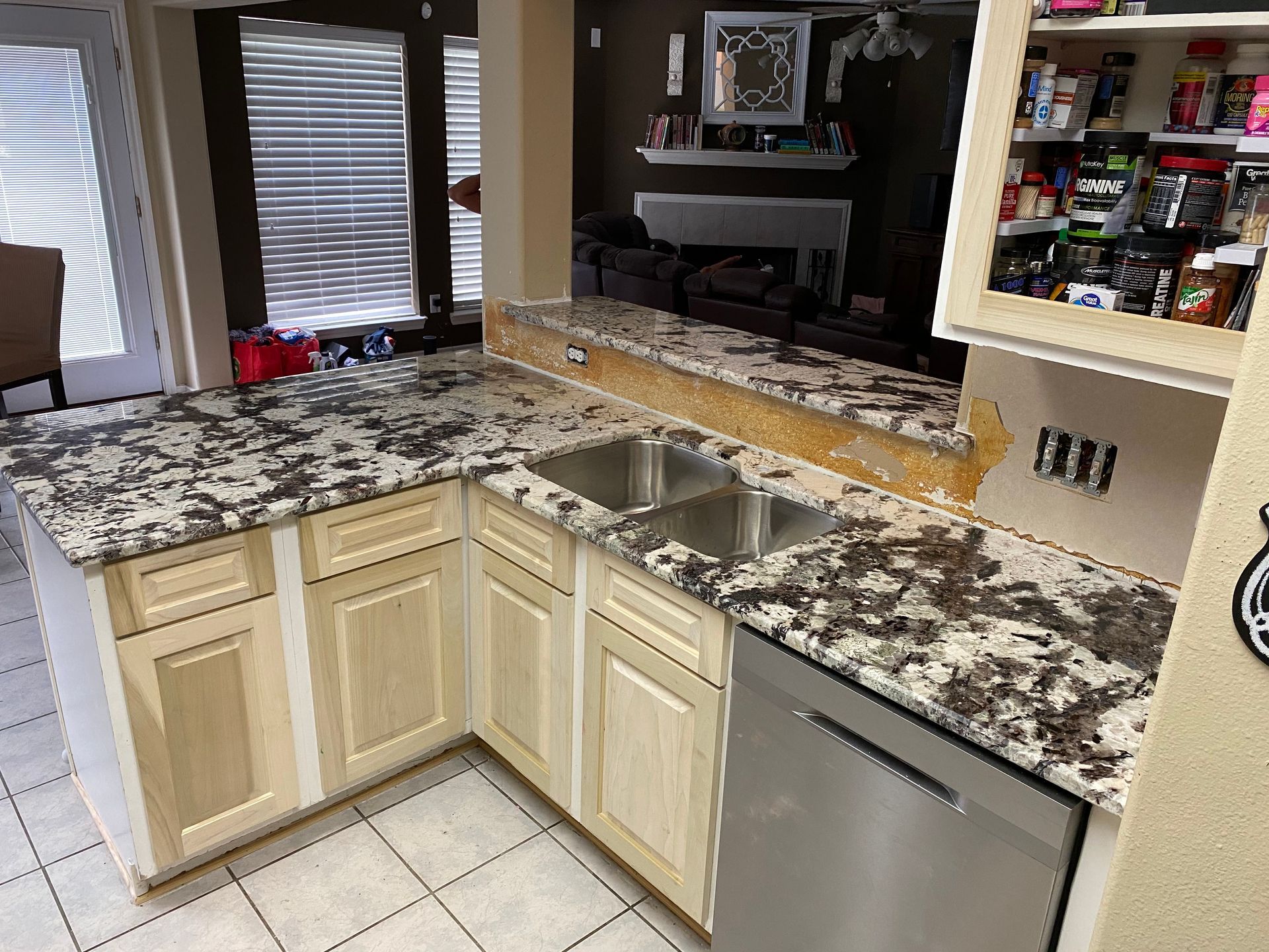 Kitchen with speckled granite countertops, cream cabinets, tiled floor, and stainless dishwasher.