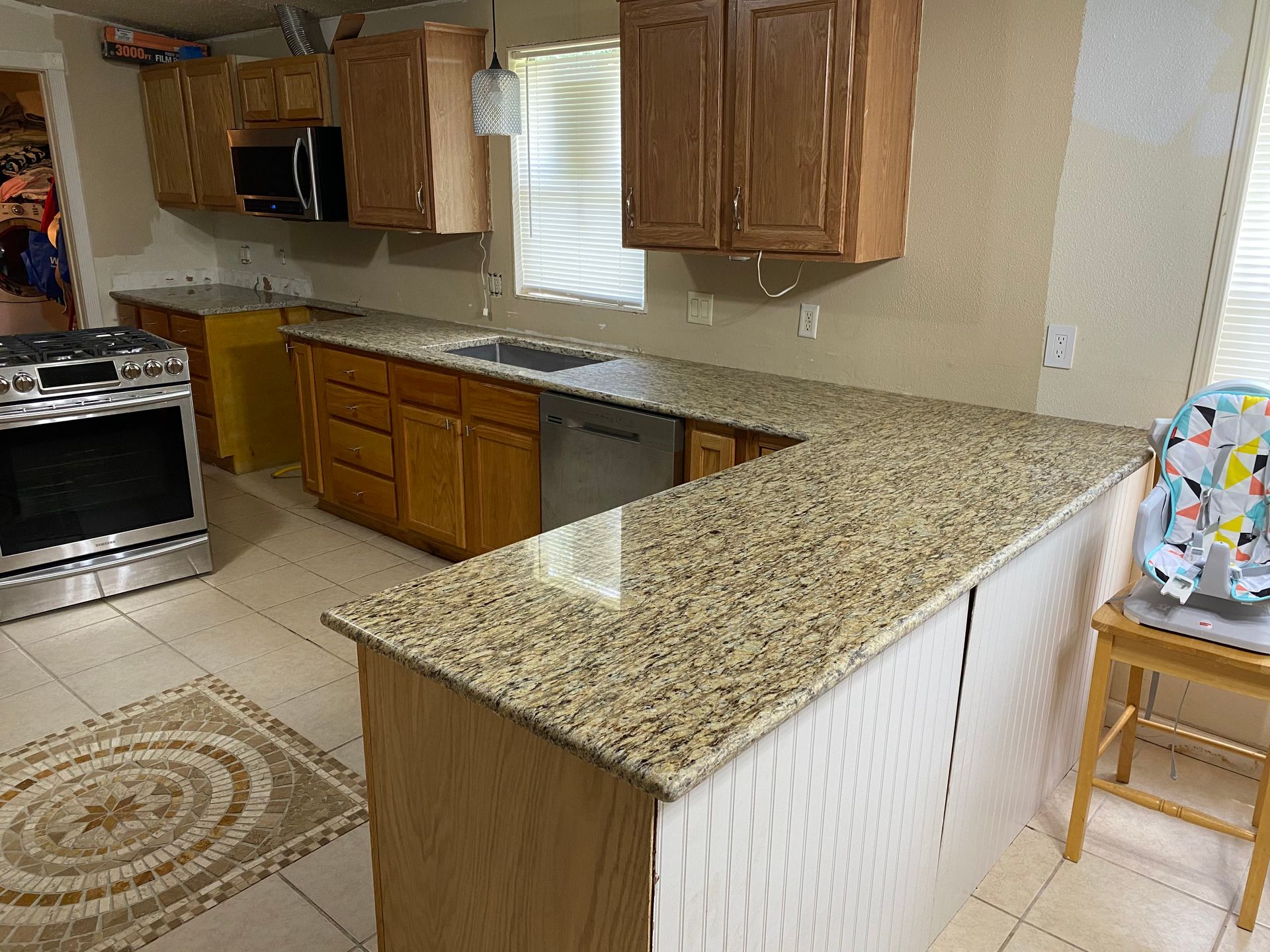 Kitchen with granite countertops, wood cabinets, stove, sink, and a patterned rug on the floor.