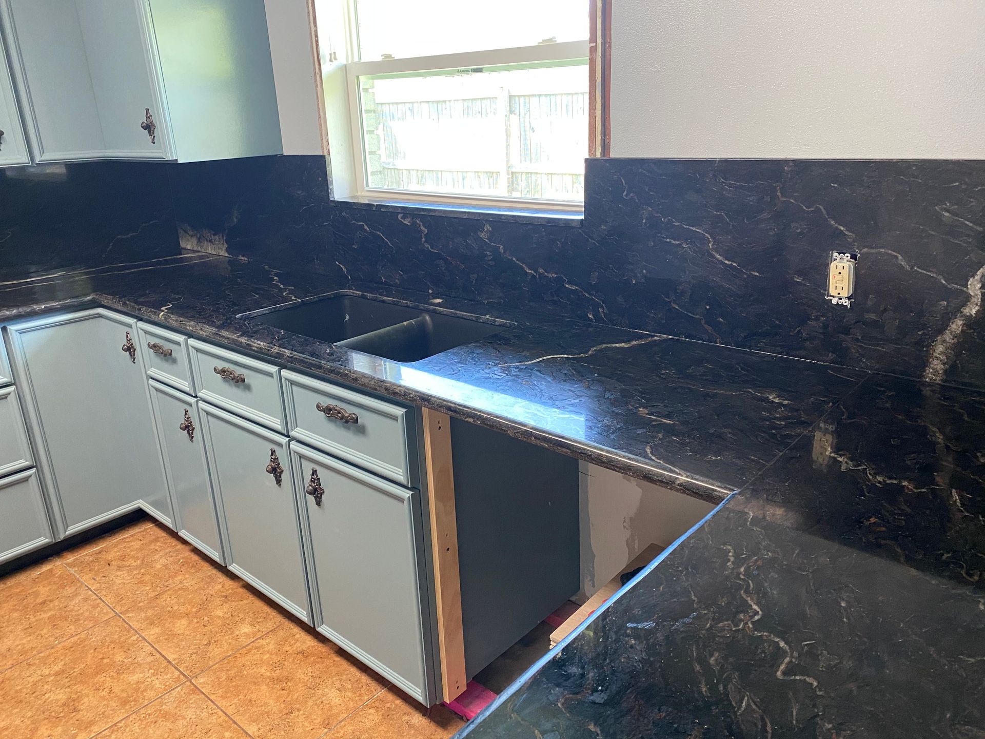 Modern kitchen with black stone countertops, white cabinets, and a window above the sink.