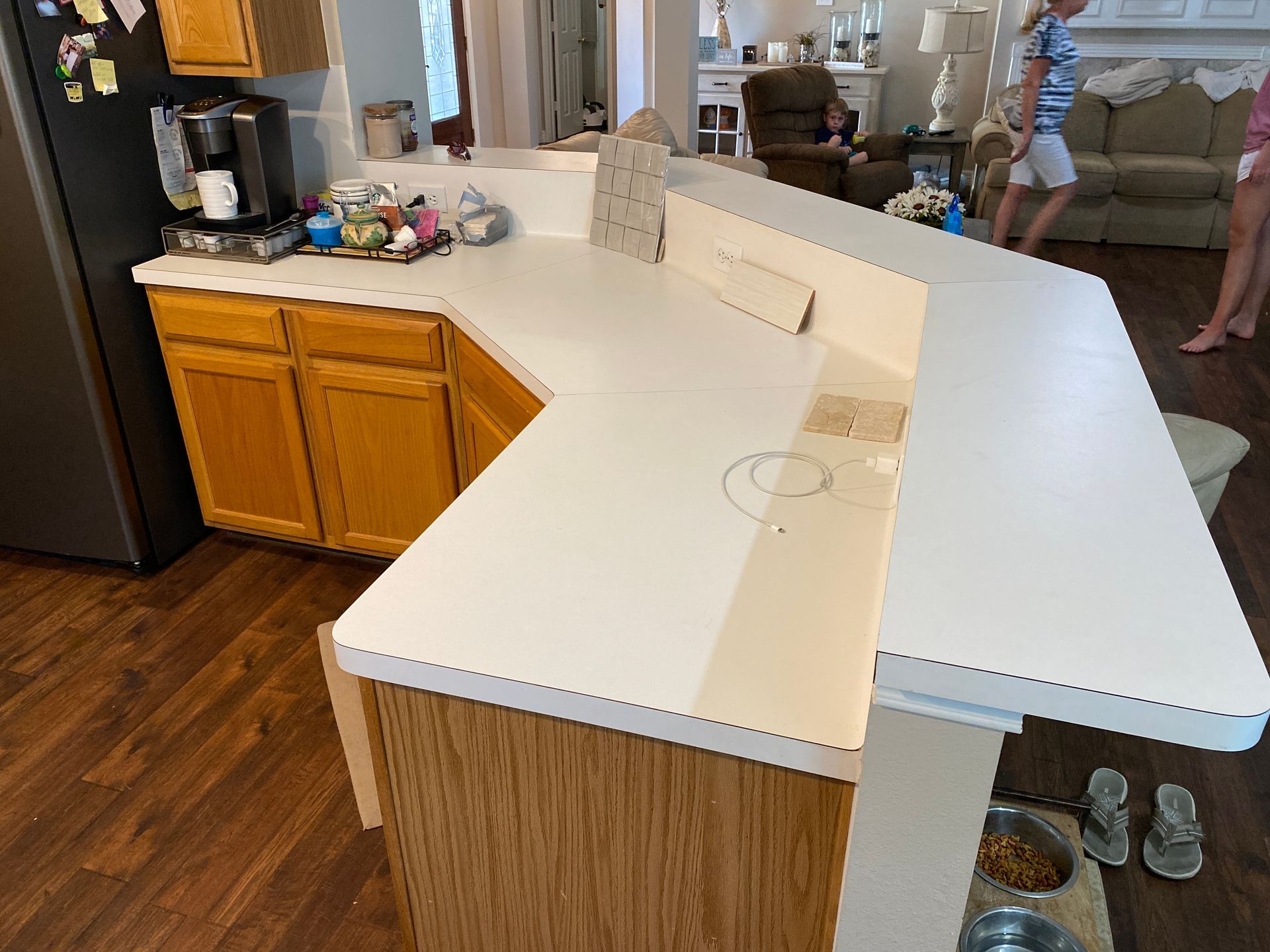 Kitchen with white peninsula counter, wood cabinets, hardwood floor, and a pair of shoes near the entrance
