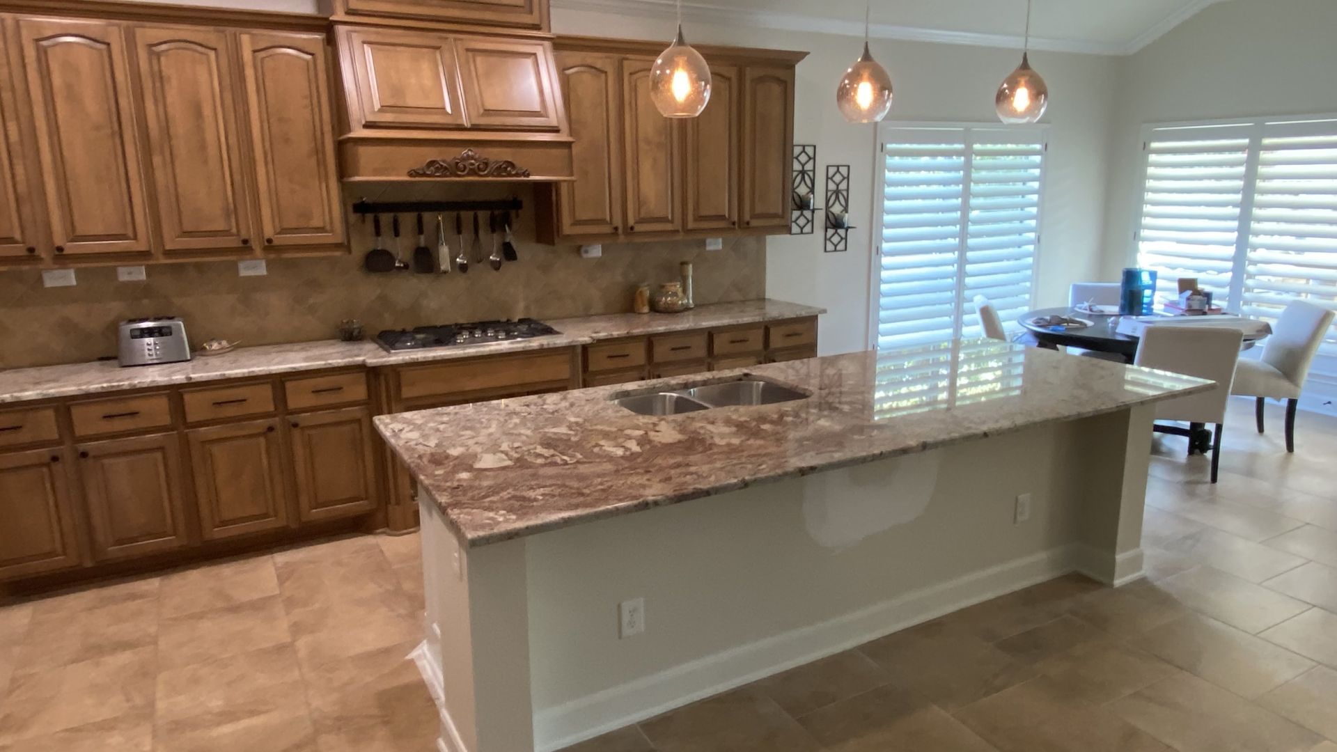 Spacious kitchen with wood cabinets, marble island, pendant lights, and dining area by a window
