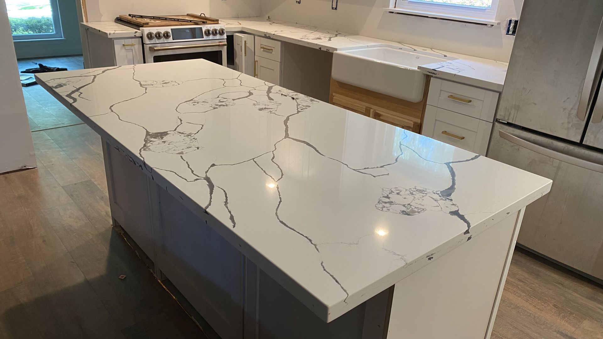 Modern kitchen with a large white marble island and white cabinets, viewed from the corner