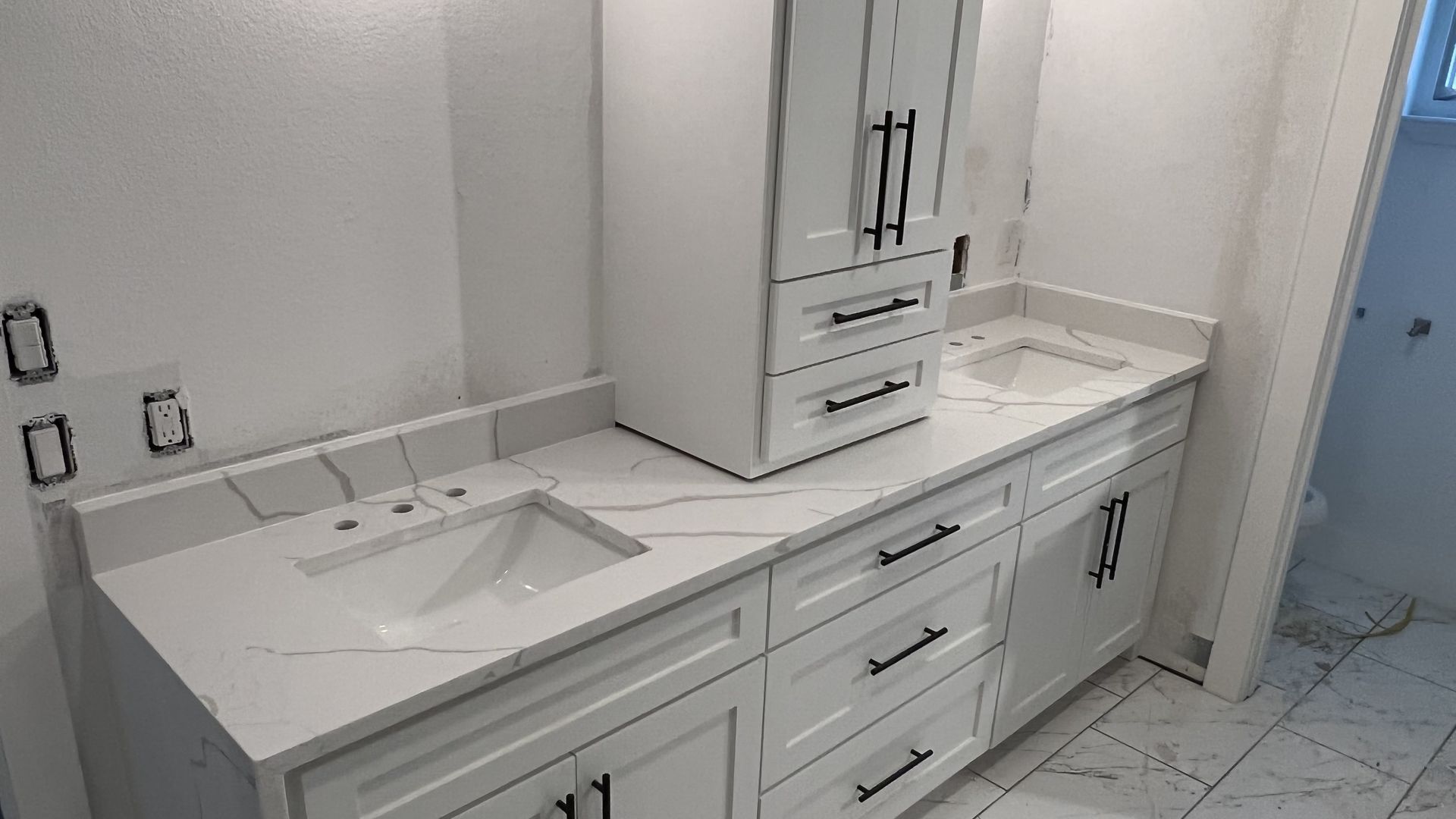 White bathroom vanity with double sinks, drawers, and a tall storage cabinet beside a tiled floor.