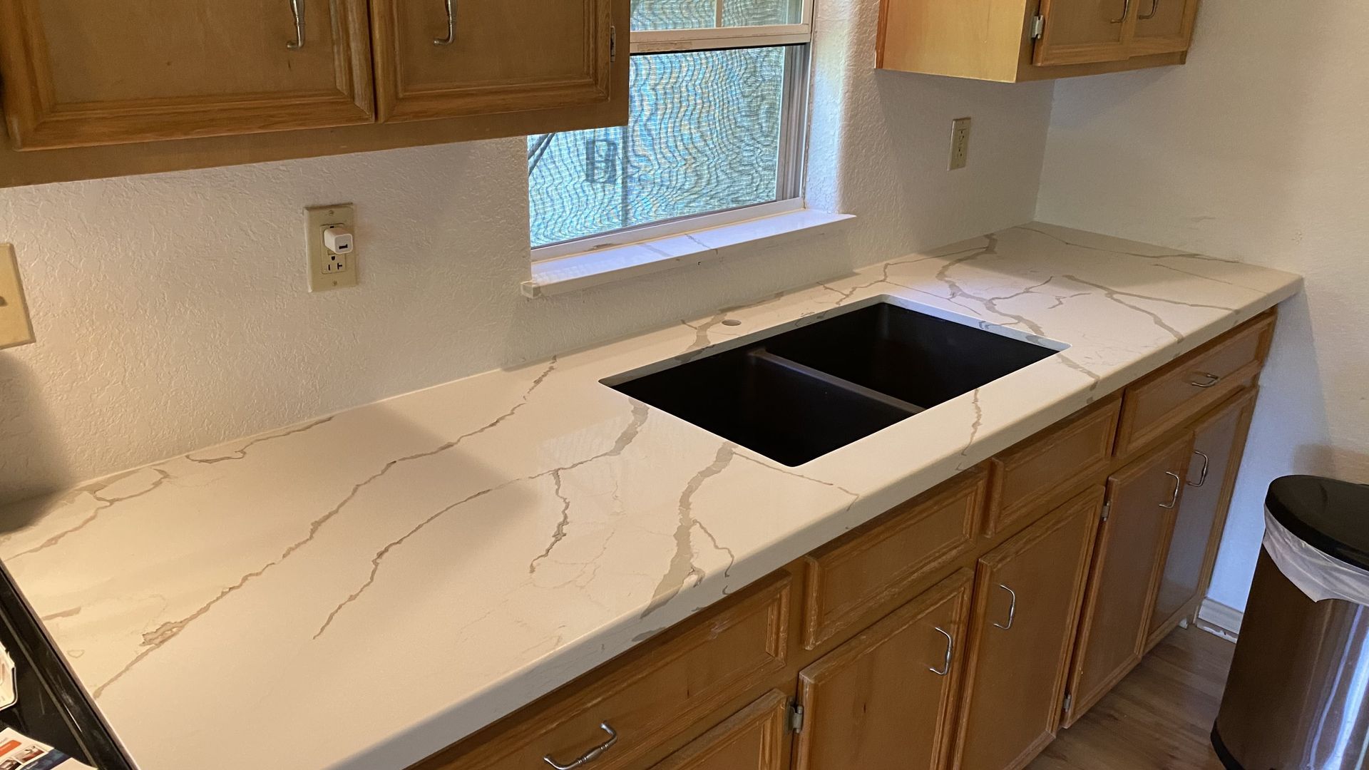 Kitchen counter with white marble-look top, undermount sink, wood cabinets, and a window above the counter