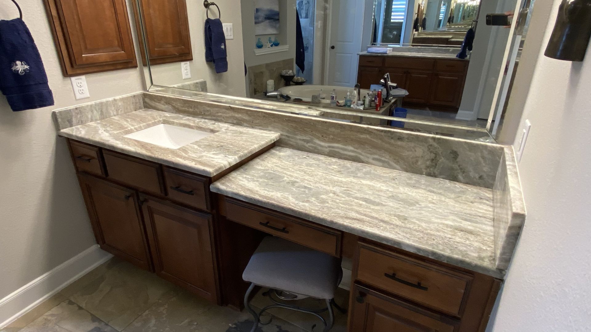 Bathroom vanity with granite countertop, double sink, large mirror, and wooden cabinets.
