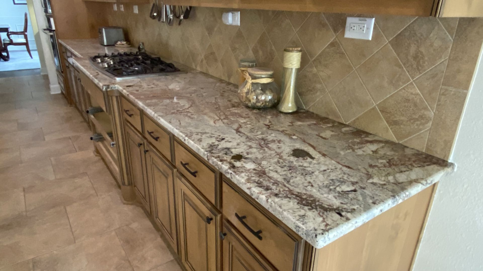 Kitchen countertop with brown cabinets, stone-look surface, stovetop, and gold decor accents