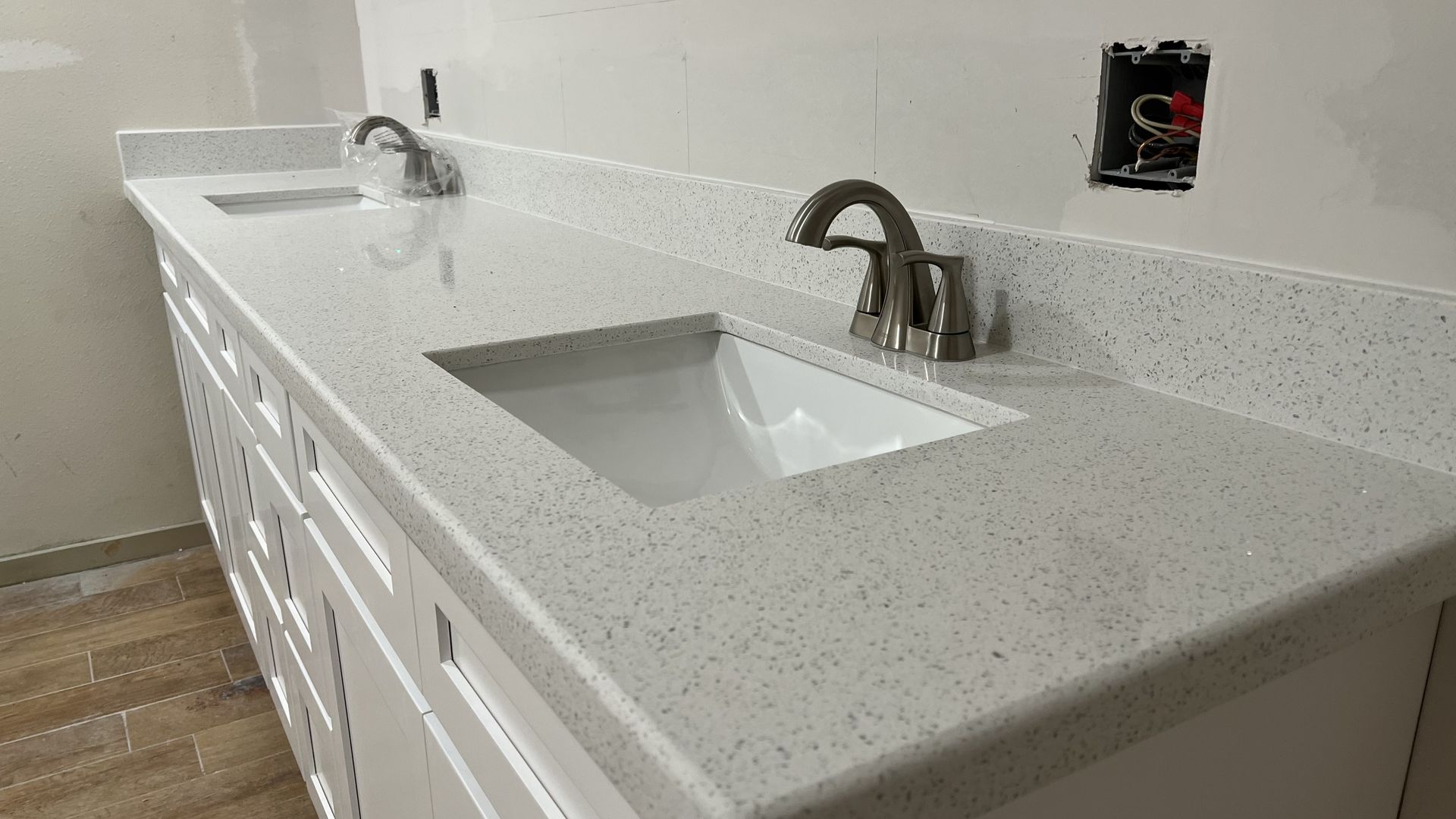 Bathroom vanity with light gray countertop, two sinks, and chrome faucets along a white wall.