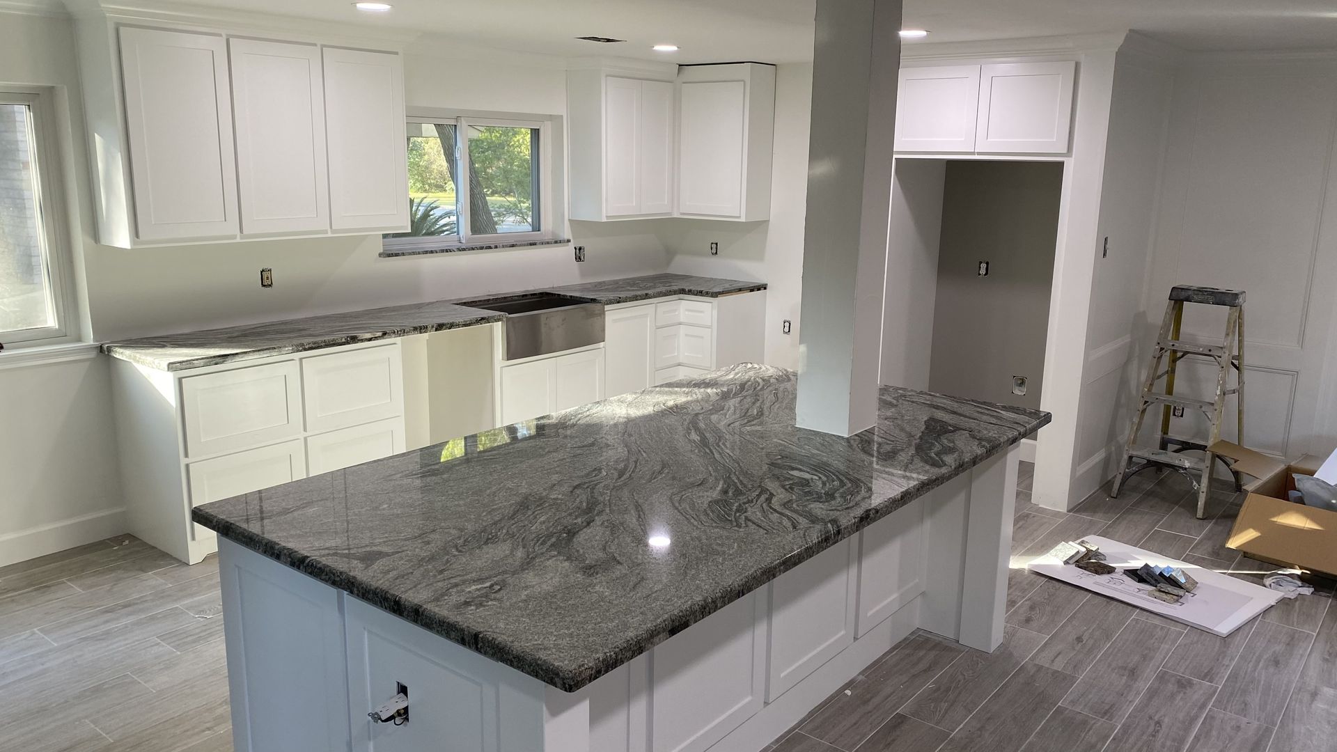 Bright kitchen renovation with white cabinets, gray island countertop, and construction materials on the floor.