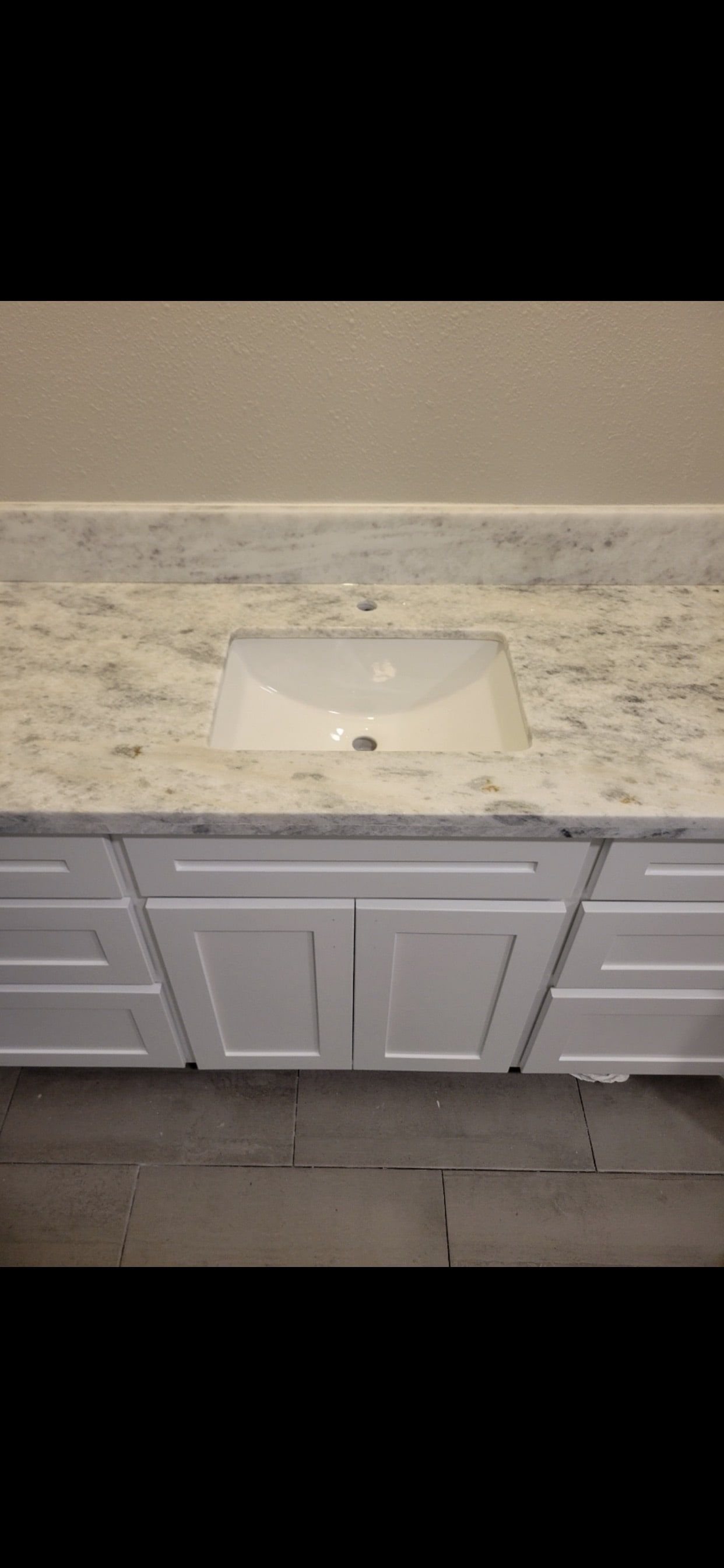 White bathroom sink and gray vanity cabinet with granite countertop and tiled floor