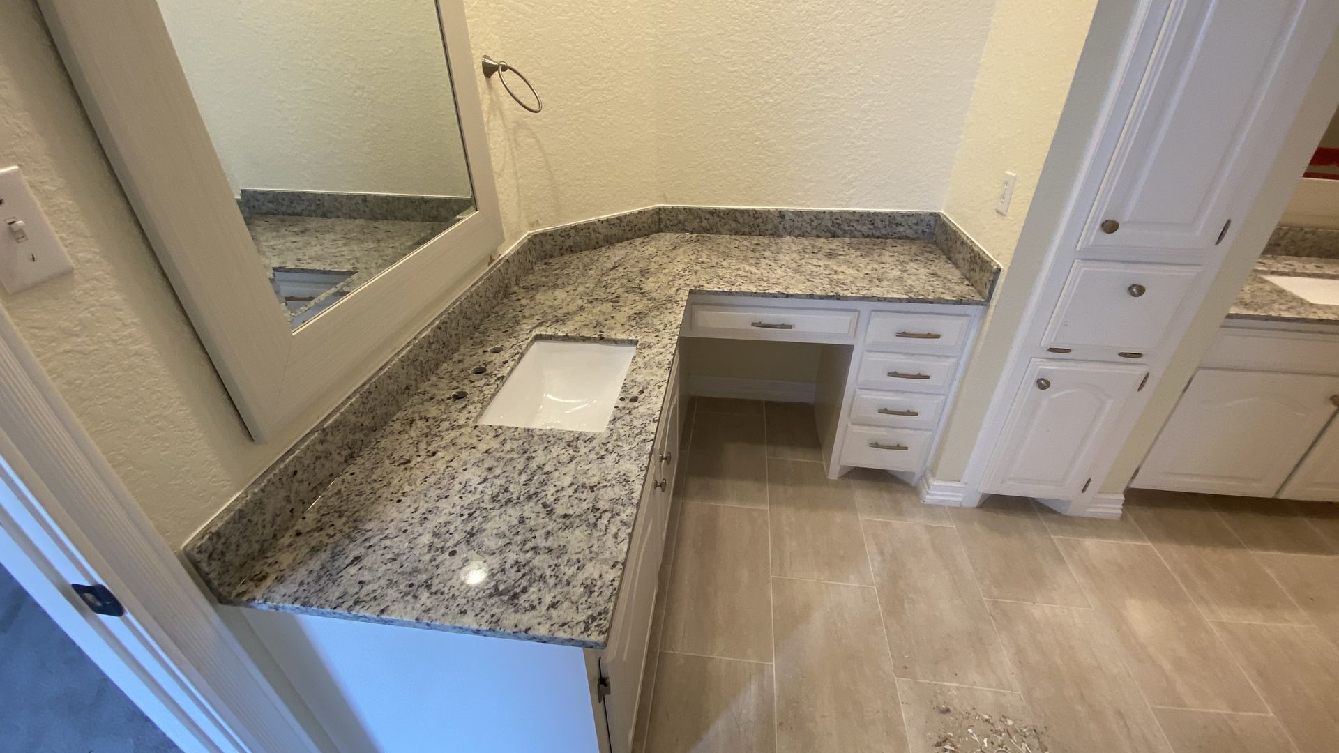 Bathroom vanity with speckled granite countertop, mirror, sink cutout, and white cabinets.