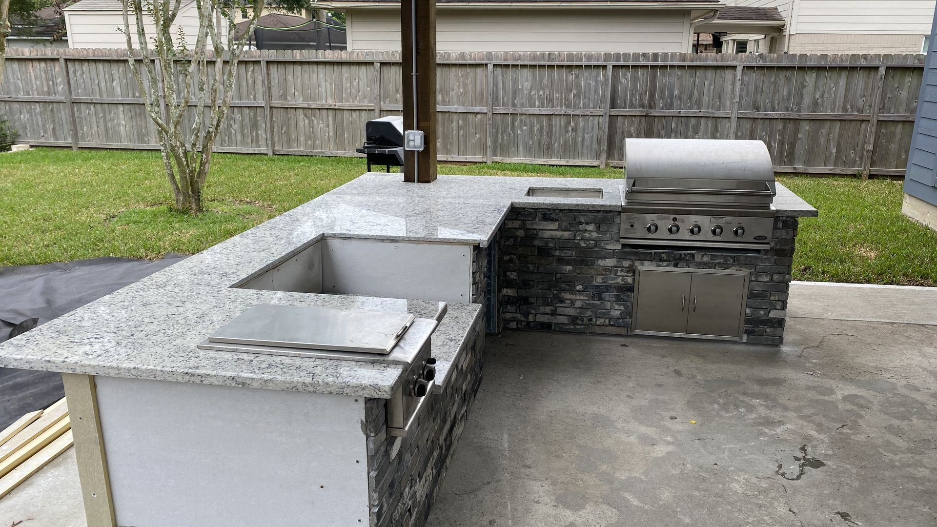 Outdoor patio with a built-in stone grill and metal barbecue smoker beside a white counter.