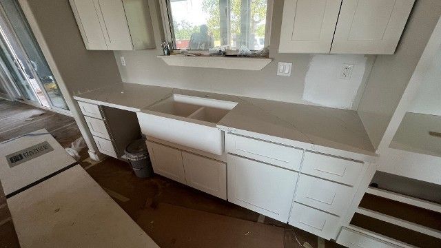 White kitchen with empty countertops, cabinets, sink under window, and built-in drawers.