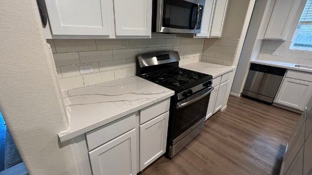 Bright kitchen with white cabinets, black stove, and wood floors.
