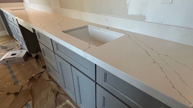 Modern white kitchen countertop with integrated sink and gray cabinets under construction