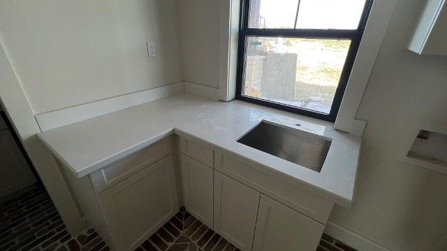 Small white kitchen corner with a sink, countertop, cabinets, and a window.