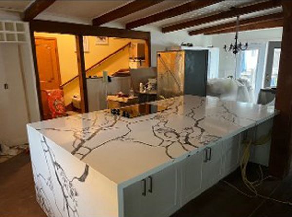 Kitchen with a large marble island, exposed ceiling beams, and stainless steel appliances in a home interior.