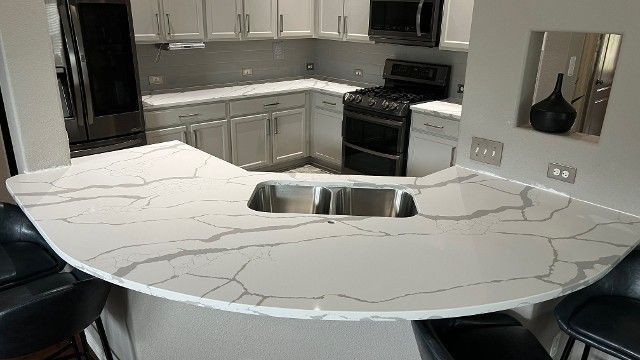 Modern kitchen with a large white marble island, stainless steel appliances, and dark bar stools.