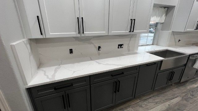 Modern kitchen with white upper cabinets, dark lower cabinets, white countertop, and stainless stove and sink