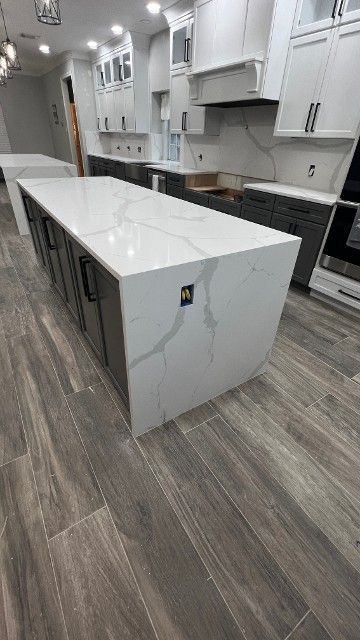 Modern kitchen with white cabinets, marble island, and gray wood flooring